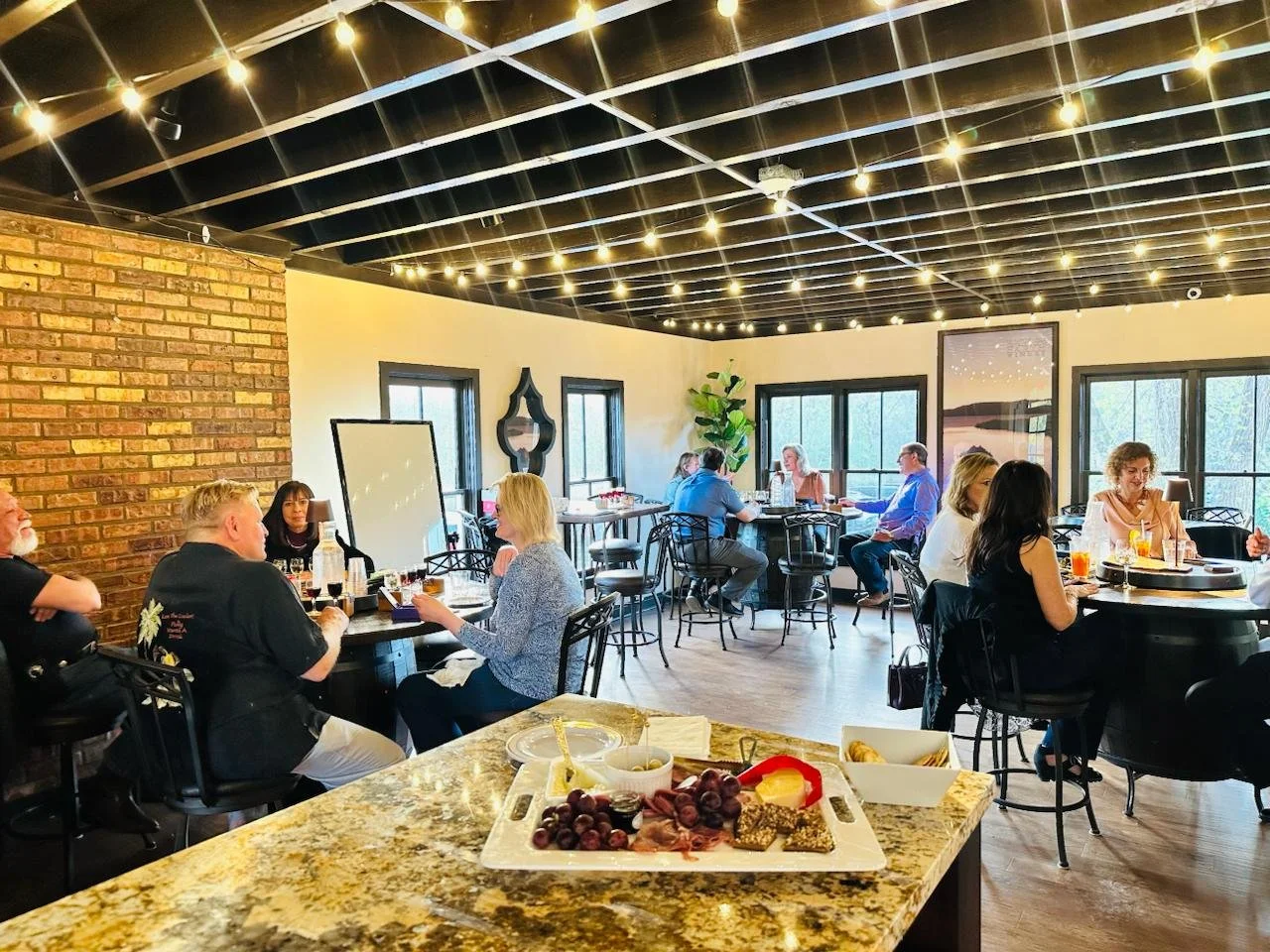 People dining in a restaurant with a string light ceiling, brick and white walls, and large windows.