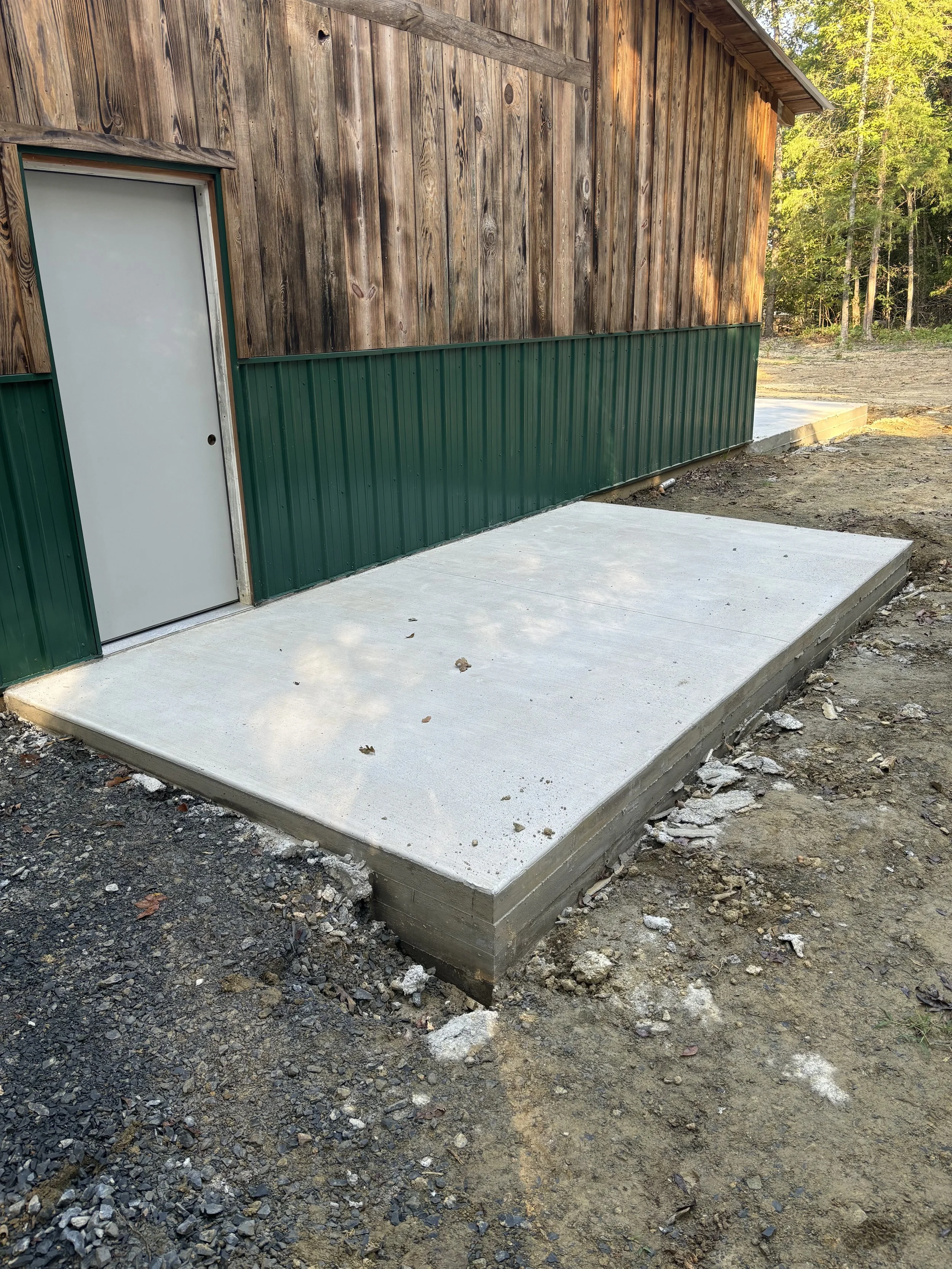 A paved concrete slab next to a wooden building with a green metal lower portion.
