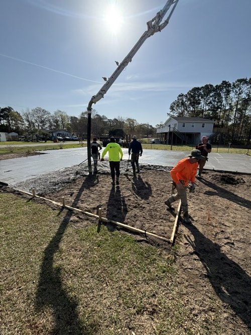 Construction workers pouring concrete foundation outdoors using a boom pump under clear skies.