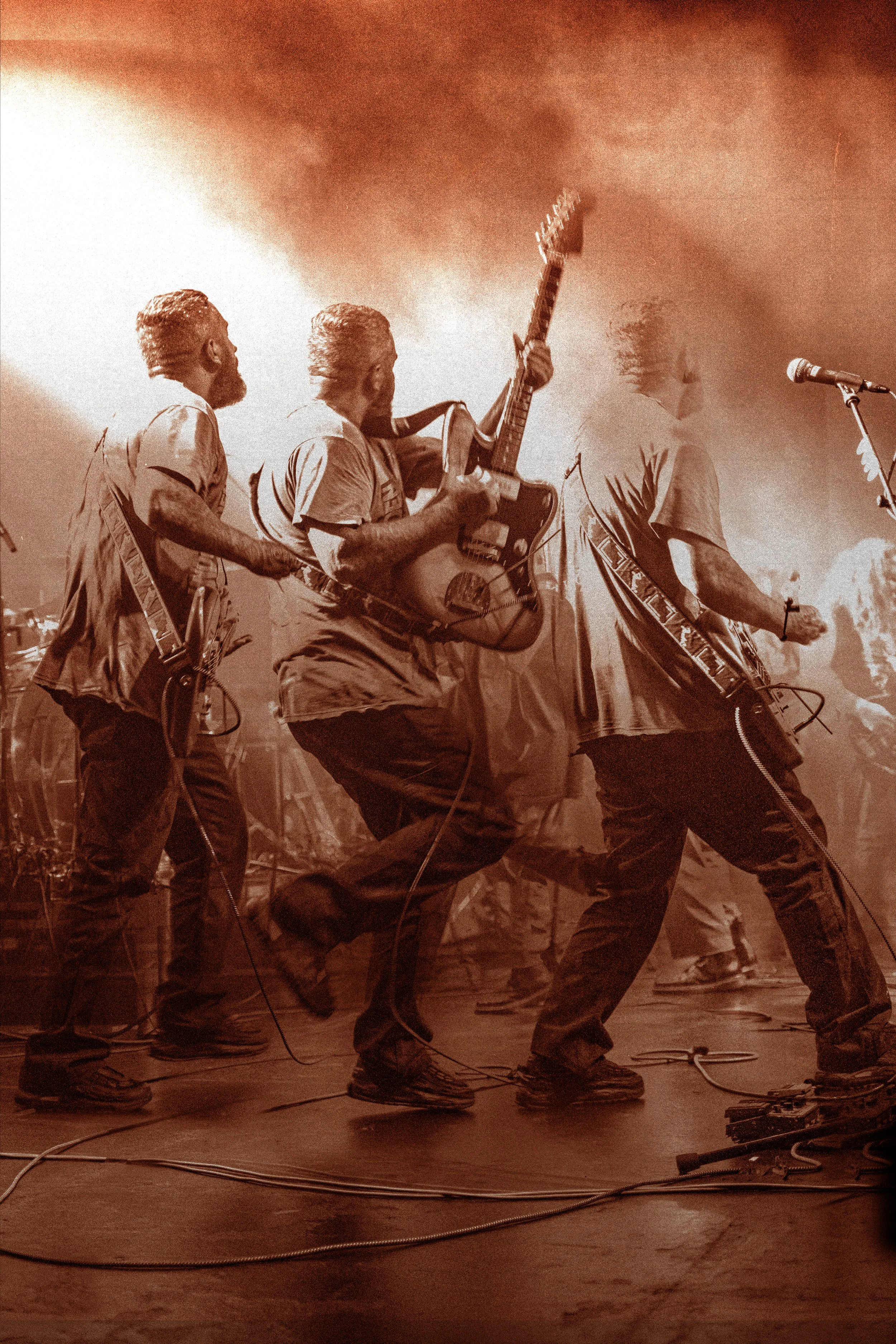 Musicians playing guitars on stage with a warm, foggy atmosphere and stage lights.