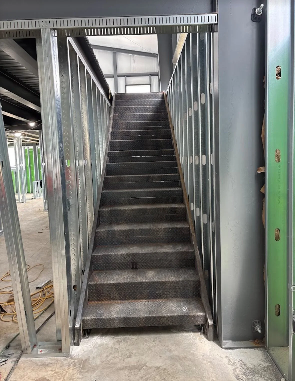 Metal staircase by A1 Metal Fabrication inside a building under construction with exposed framing and electrical wiring.