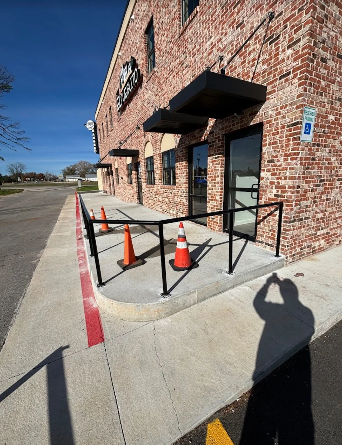 Sidewalk outside a brick building with black canopy awnings and orange traffic cones, indicating a wheelchair accessible ramp with a handrail by A1 Metal Fabrication.