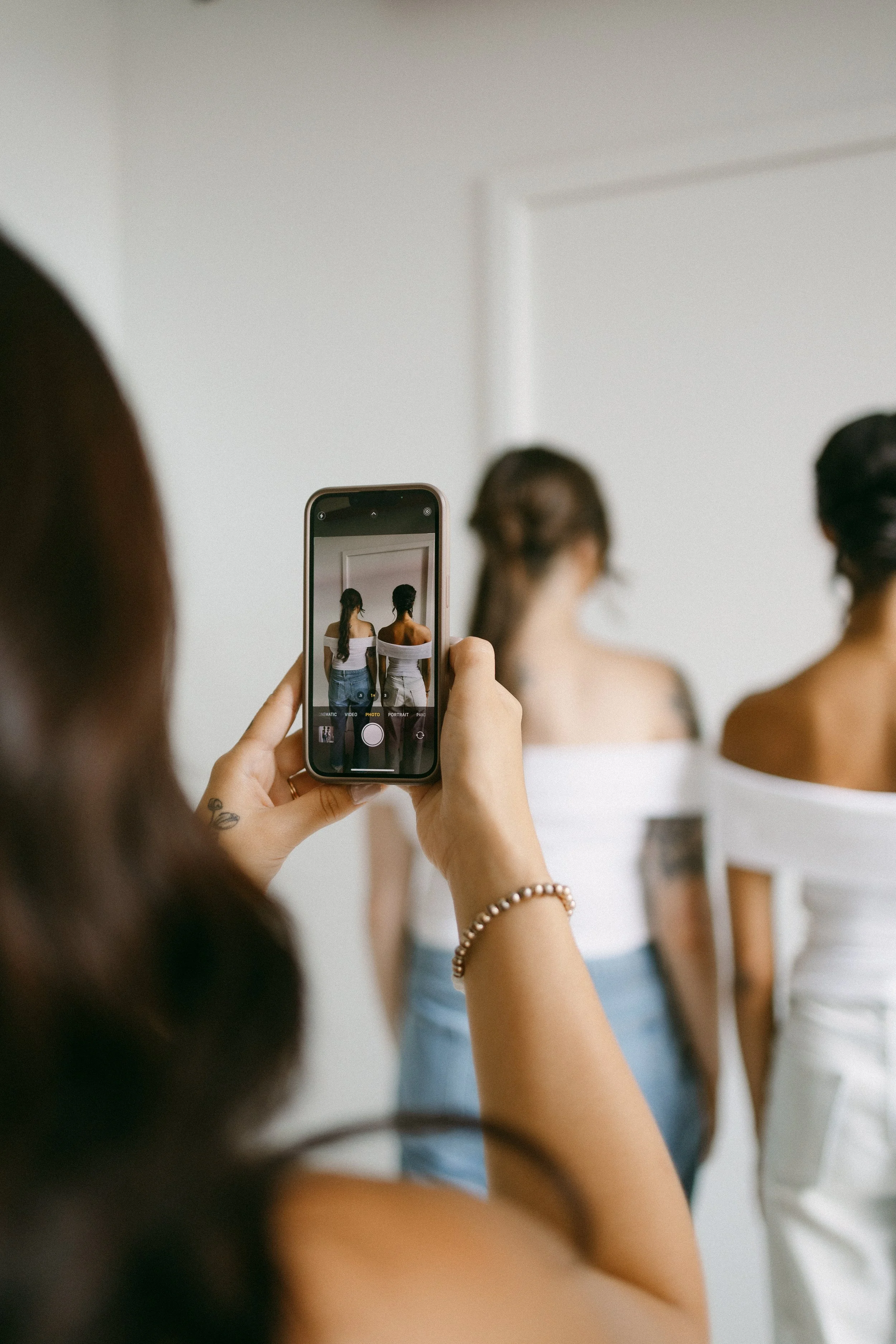Person taking a photo on their phone of two women standing in front of a white wall.