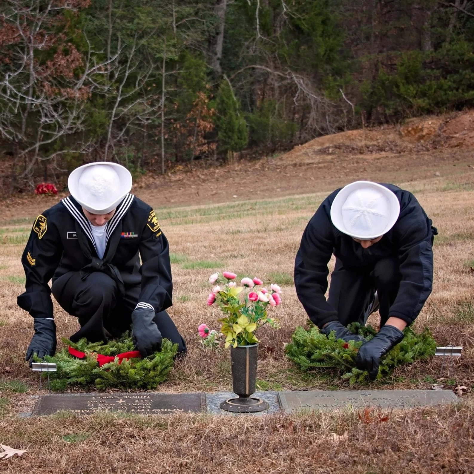 Two uniformed Sea Cadets kneeling at gravesite, laying wreaths and flowers for Wreaths Across America.