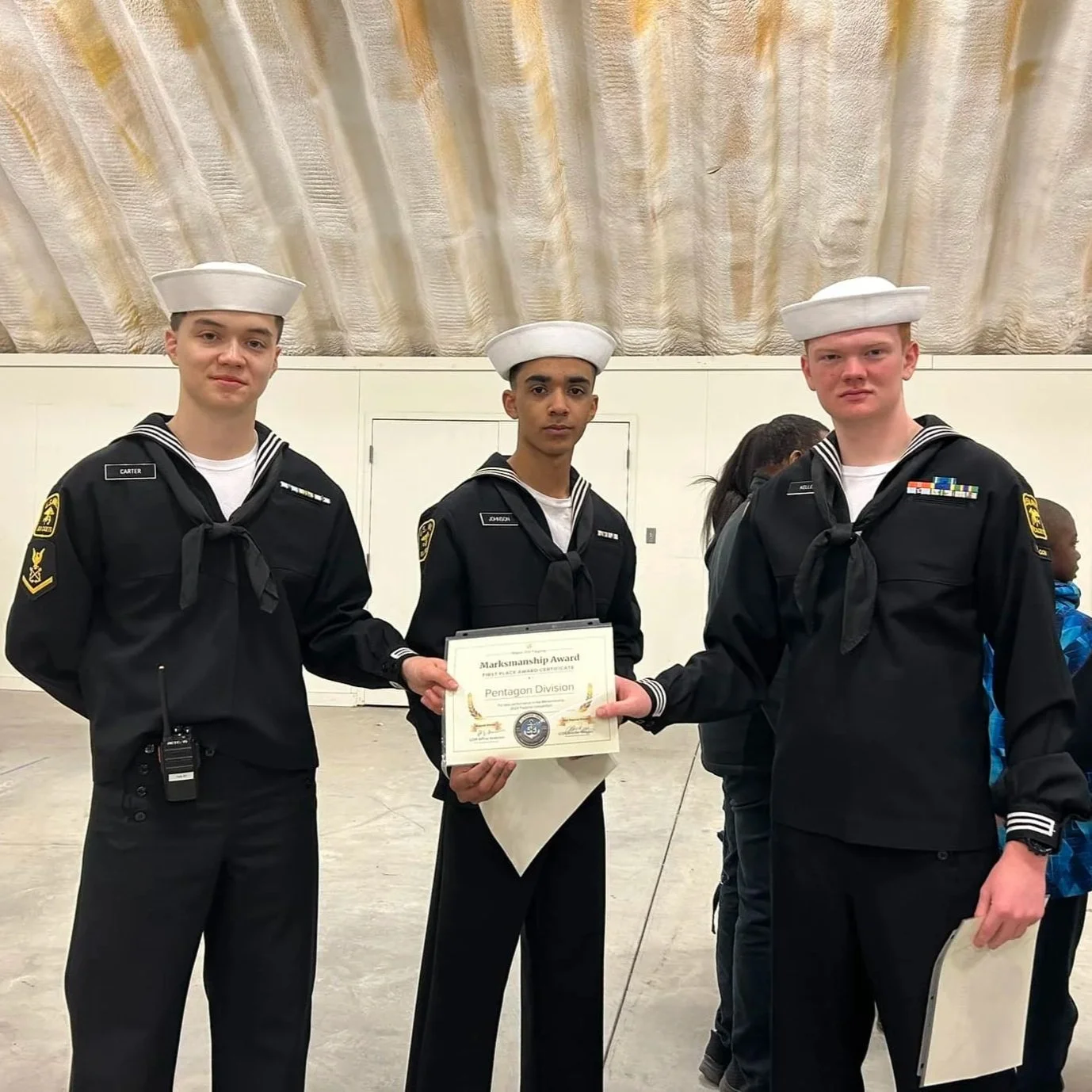 Three young men dressed in Sea Cadet uniforms, with white sailor hats, holding a certificate of merit. They are participating in a military or naval program awards ceremony.