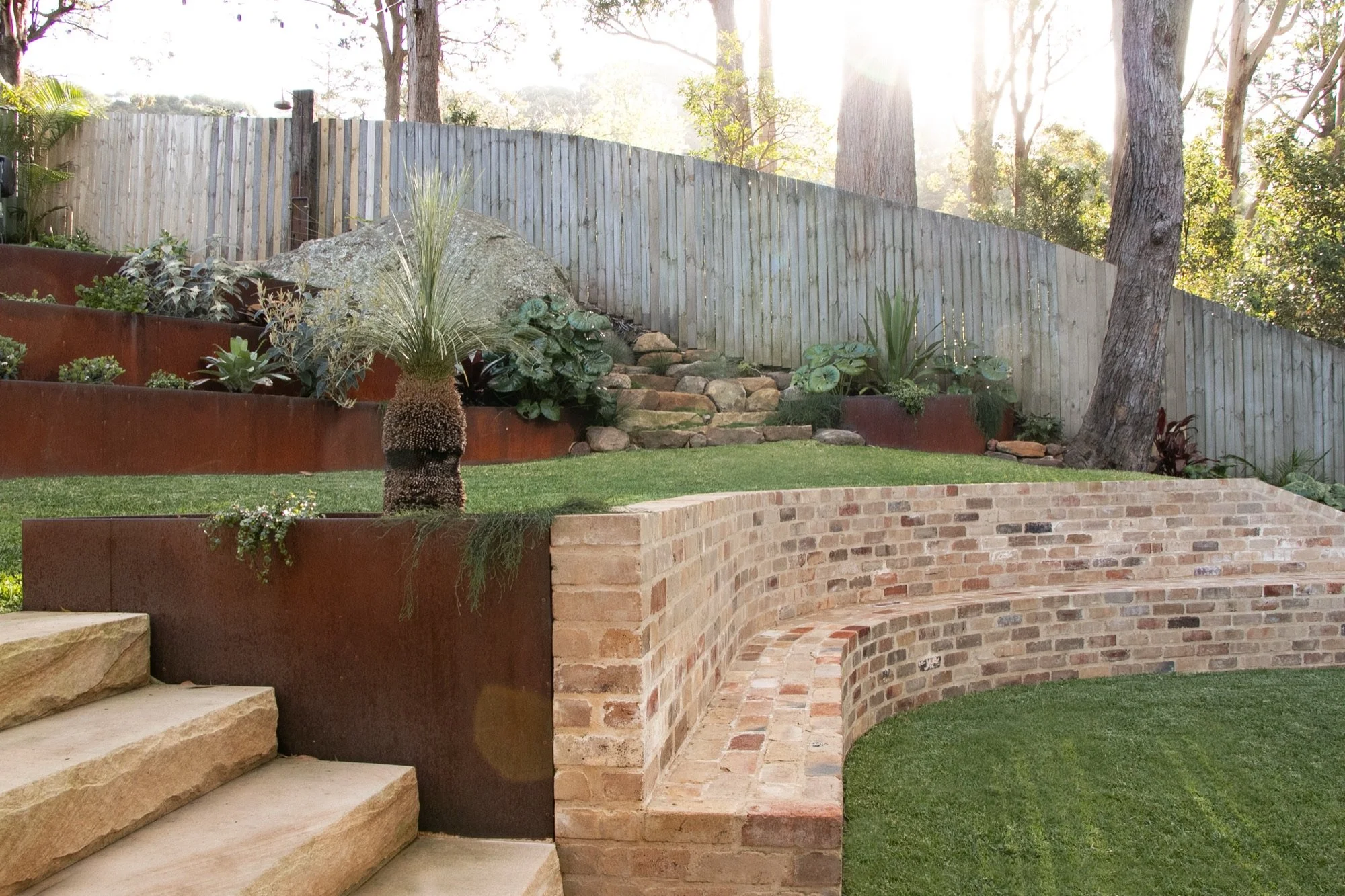 Sandstone steps leading to a curved recycled brick retaining wall and lawn in Bulli