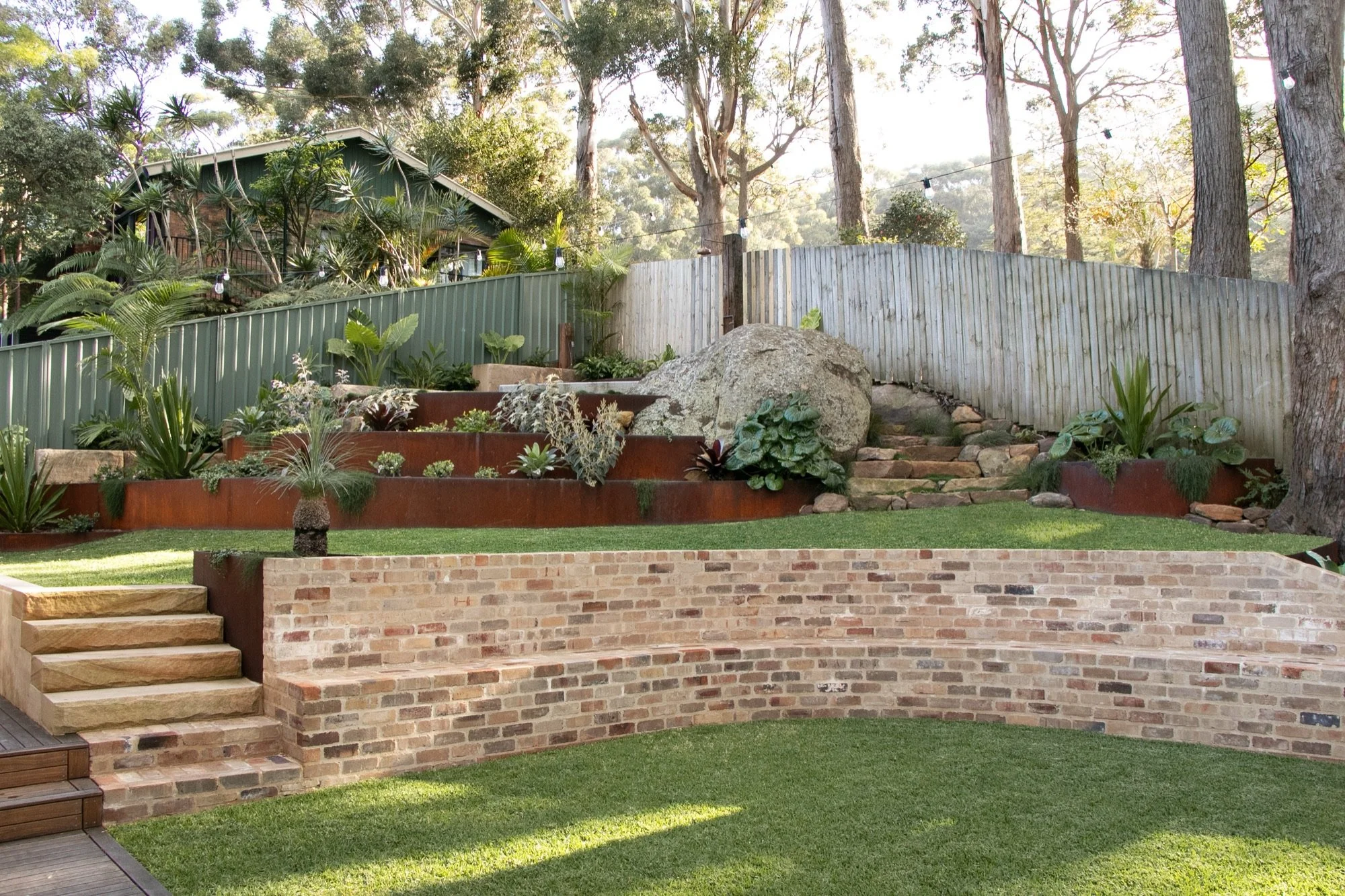 Four-tier landscaped slope with corten walls, sandstone stairs and a recycled brick bench in Bulli