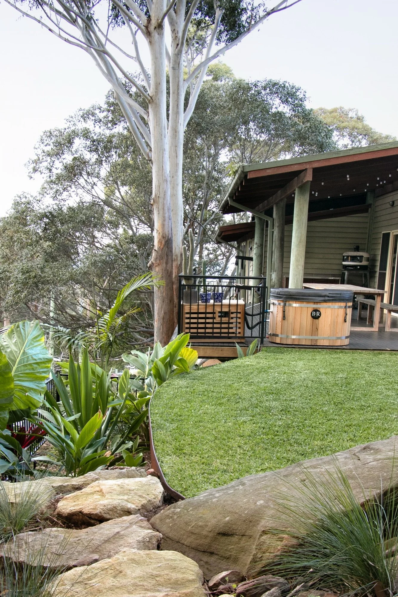 Spa deck above a curved lawn terrace with sandstone boulders and tropical planting in Bulli