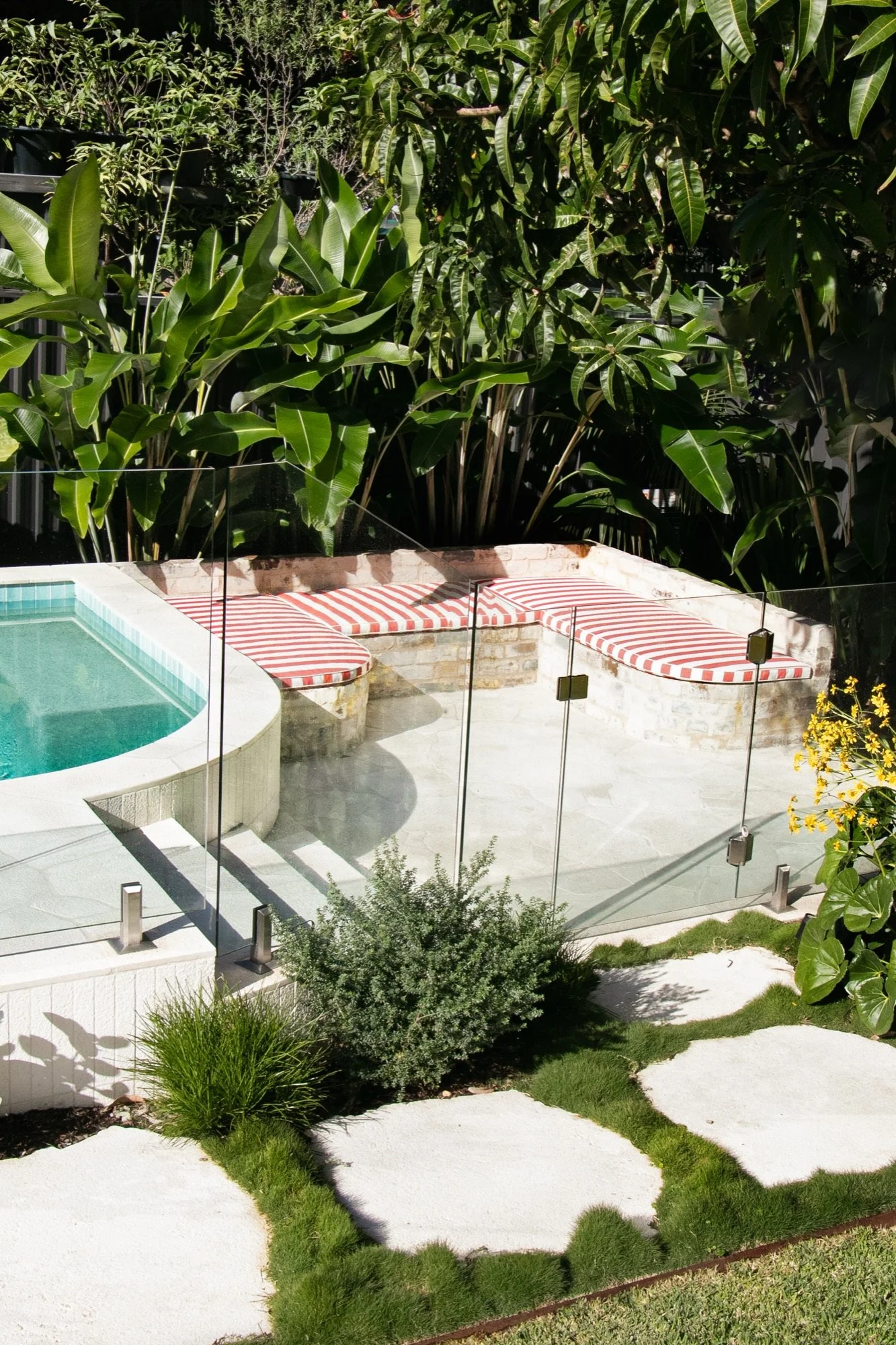 Poolside relaxation zone with striped cushions behind glass pool fencing in Chifley