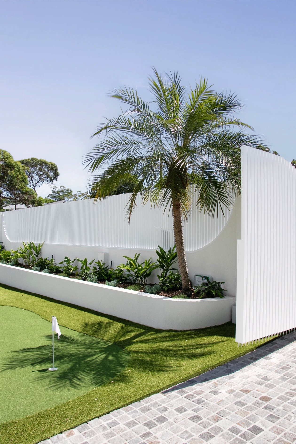 Palm tree and layered planting along the white privacy wall beside the putting green, showing detailed landscaping within this Port Hacking project.
