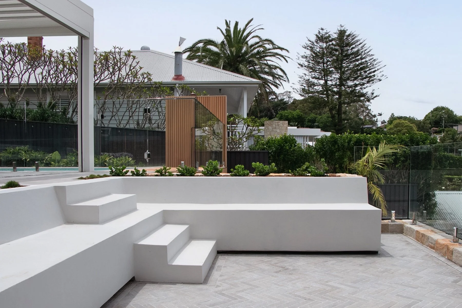 Luxury sunken outdoor seating area with white rendered retaining walls and tiled patio by Sydney landscapers