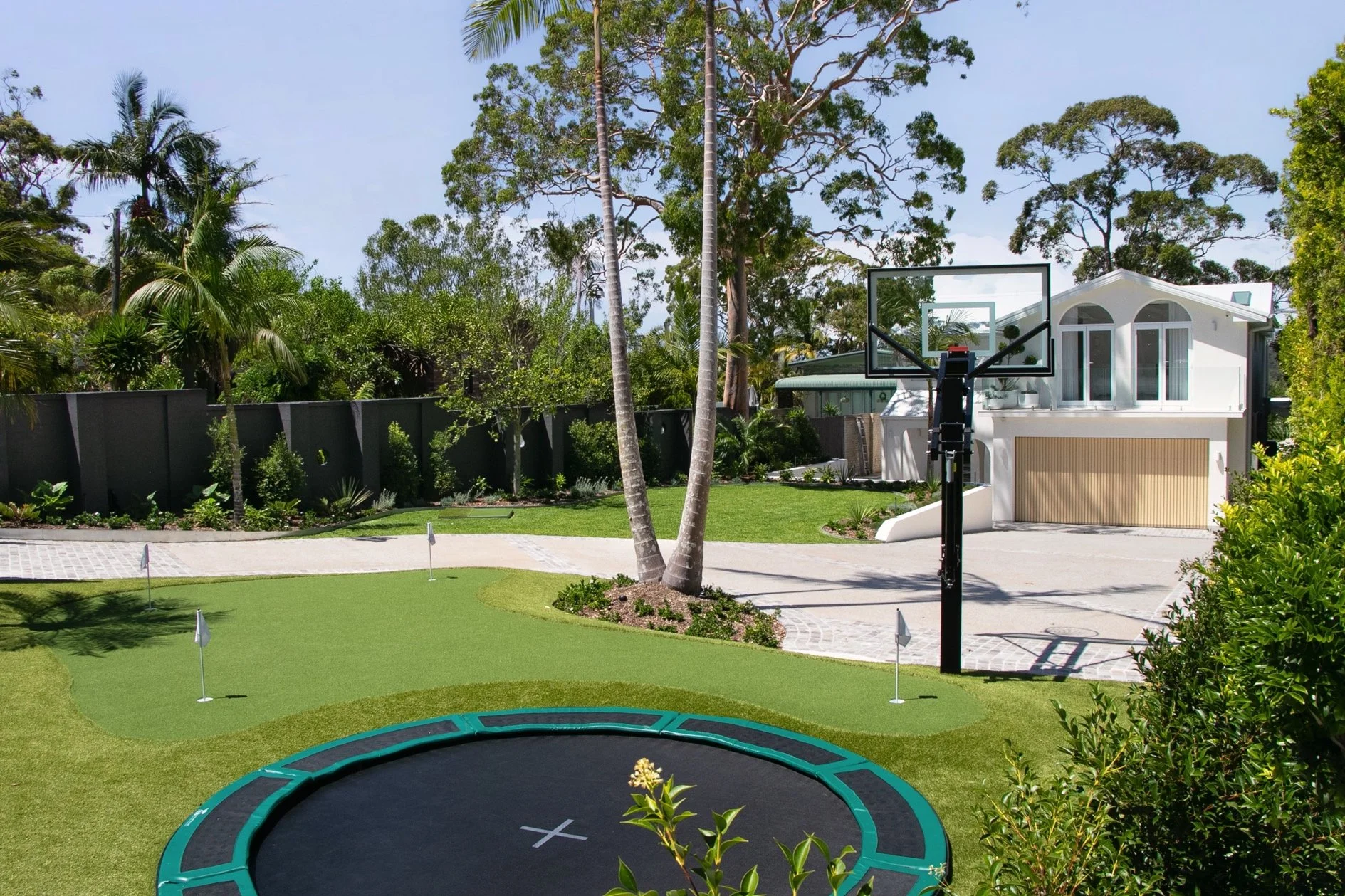 Putting green outlook toward the dark boundary wall and layered tropical planting, capturing the depth of the landscaping work on this outdoor transformation.