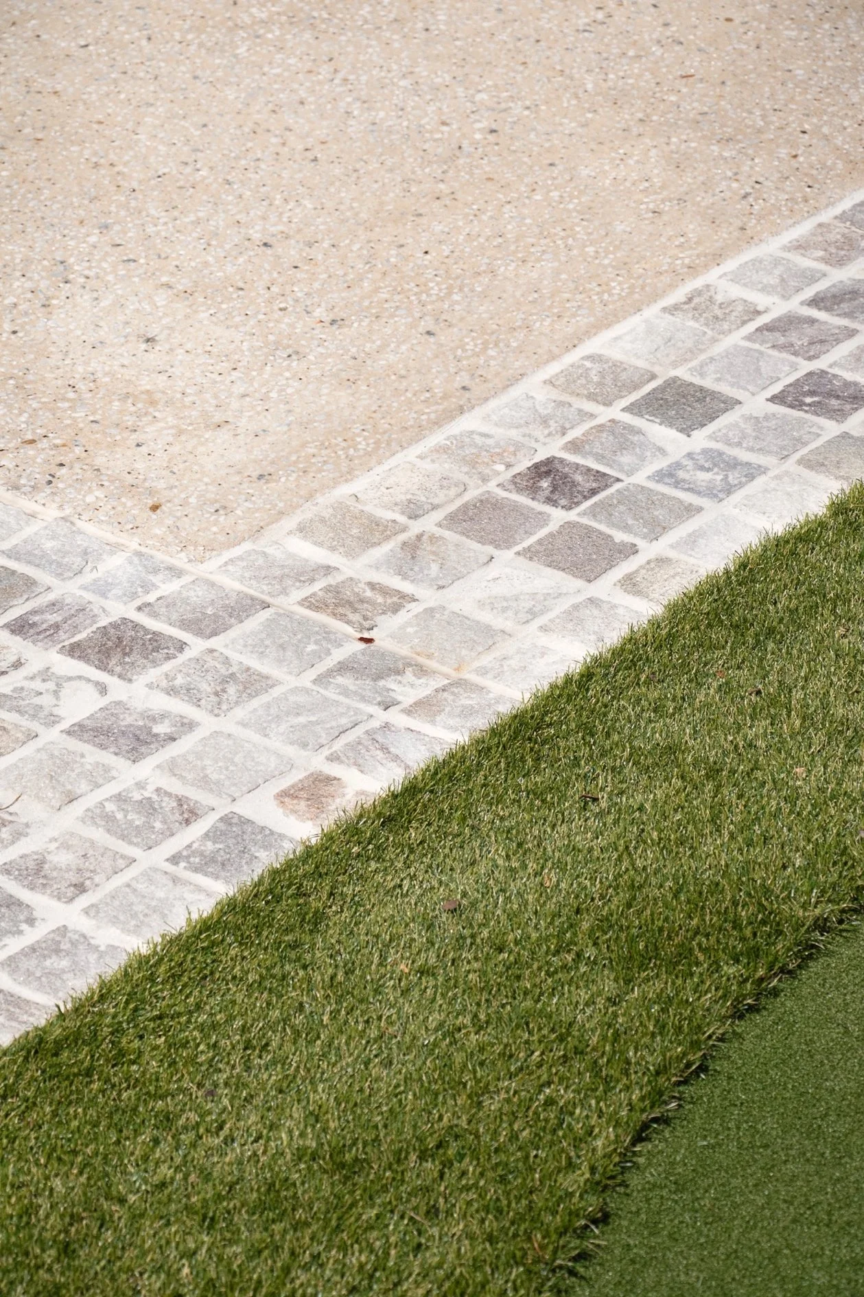 Close detail of the custom concrete driveway finish showing exposed aggregate beside cobblestone edging and turf, part of the wider outdoor transformation.