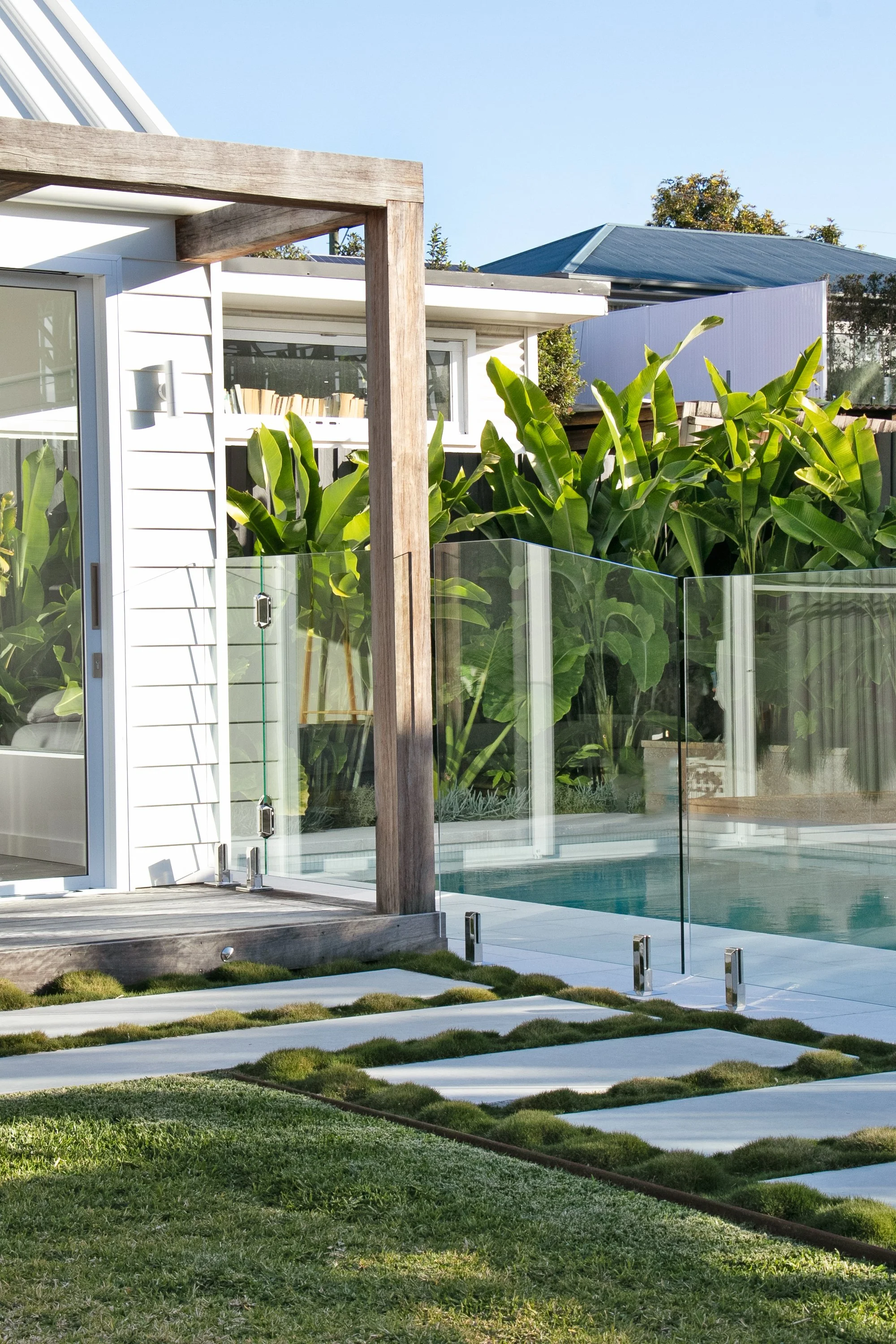 Landscape renovation of a backyard with a small swimming pool, glass safety fence, tropical plants and a pool house build in North Manly, Sydney