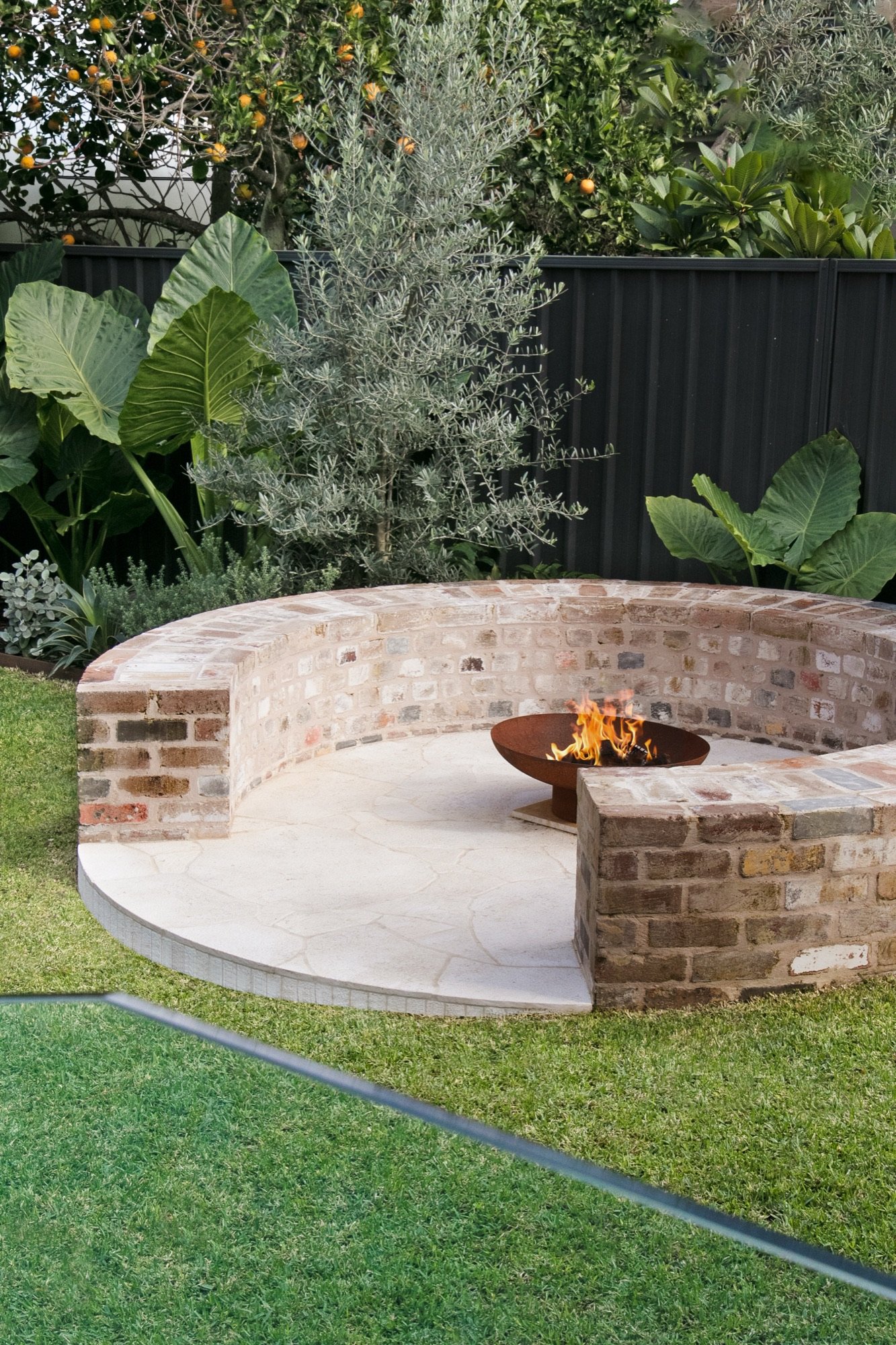 Circular recycled brick fire pit with sandstone floor and lush planting in Chifley