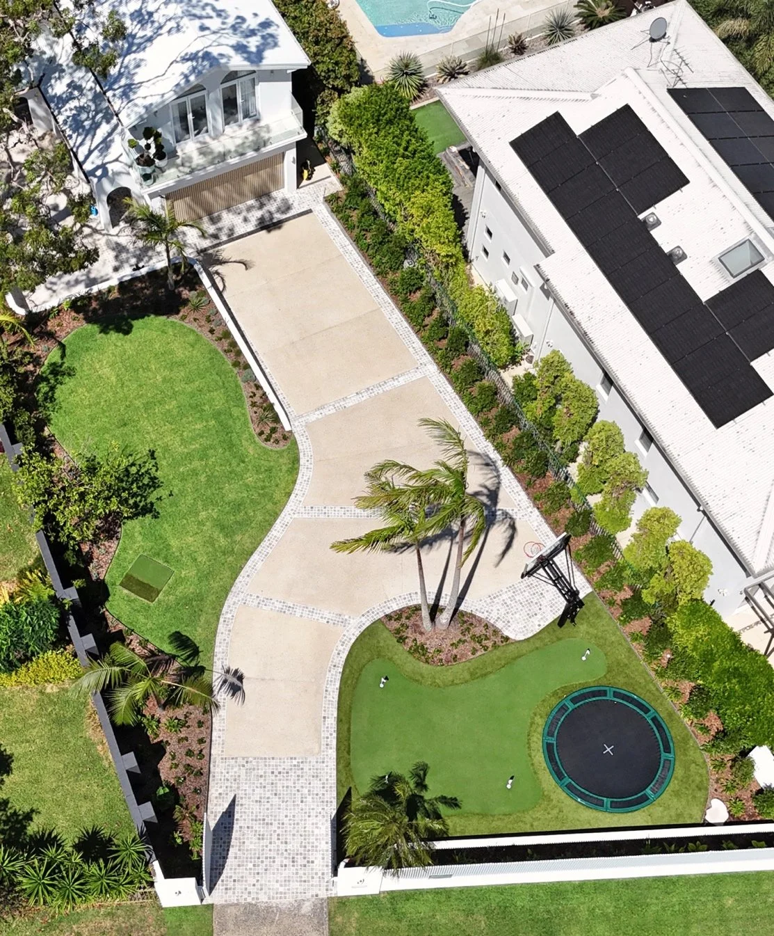 Aerial view of the full front yard in Port Hacking showing the shaped driveway, curved lawn, established palms, landscaped beds, putting green and in ground trampoline.