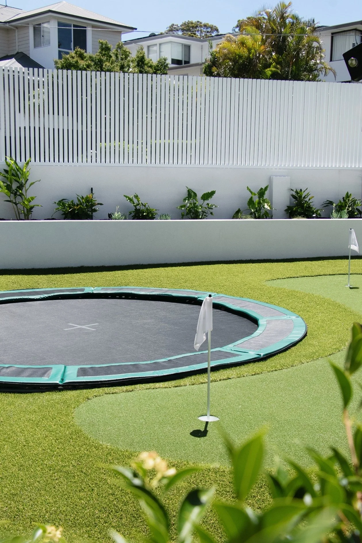synthetic putting green with two holes, in-ground trampoline, australian plant palette and stainless steel batten fence inside recently landscaped space in Sutherland Shire