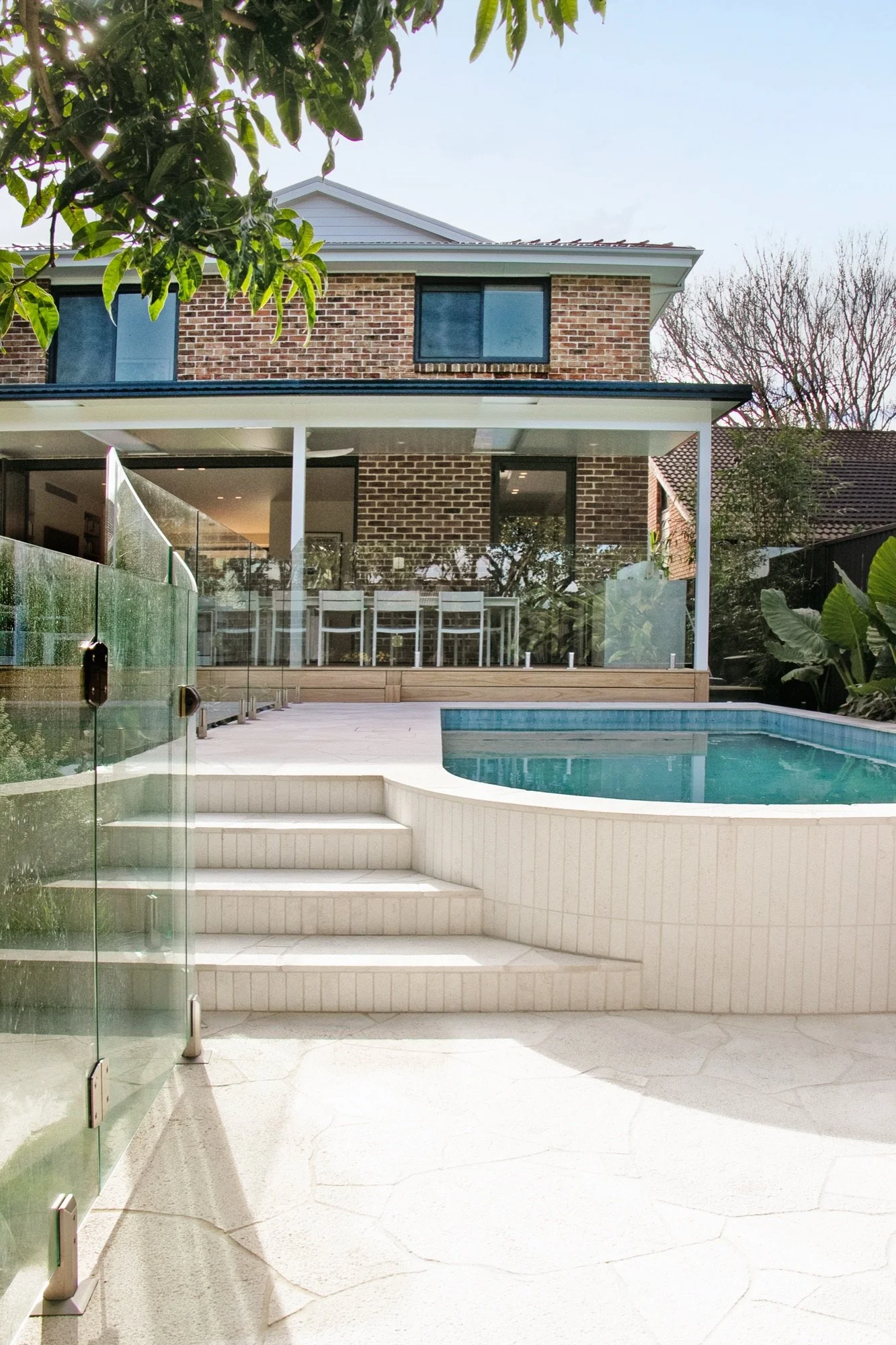 Curved concrete pool and wide stone steps leading up to the renovated home in Chifley