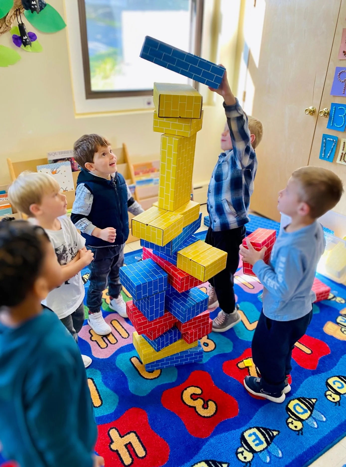 Children playing with large colorful foam blocks to build a tower in a classroom.