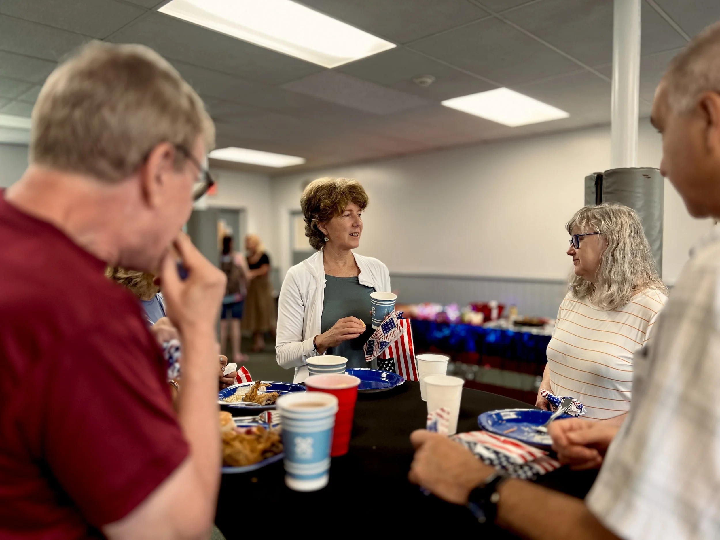 Group of people having a conversation at a table with patriotic decorations and food during a gathering or celebration.