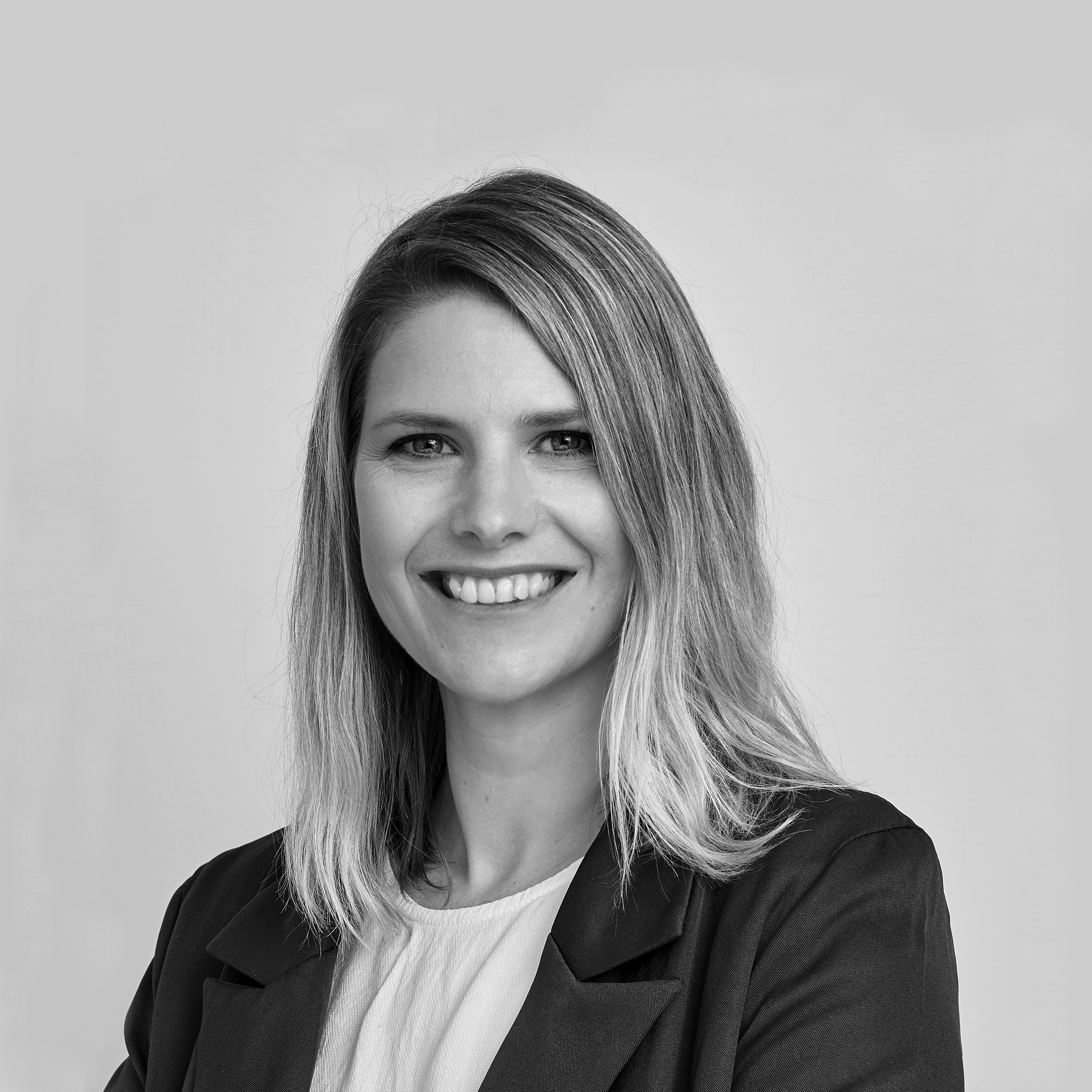 Black and white professional headshot of a smiling woman with shoulder-length hair, wearing a blazer and a light-colored top, against a plain light background.