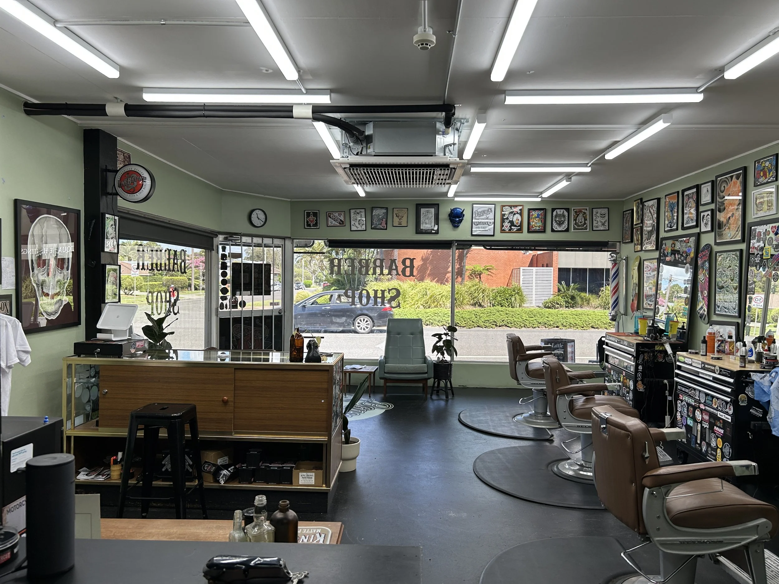 Commercial Air Conditioning. Interior of a barbershop with multiple barber chairs, a large window, and wall art. Port Macquarie, NSW