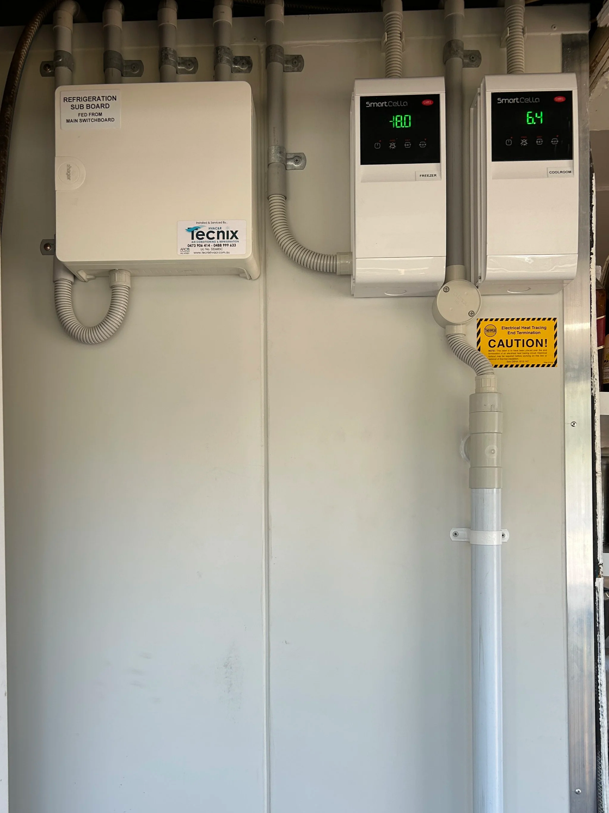 Electrical panel with two digital displays showing temperature readings, one labeled 'Freezer' and the other 'Coolroom,' with a warning sign about heat tracing.