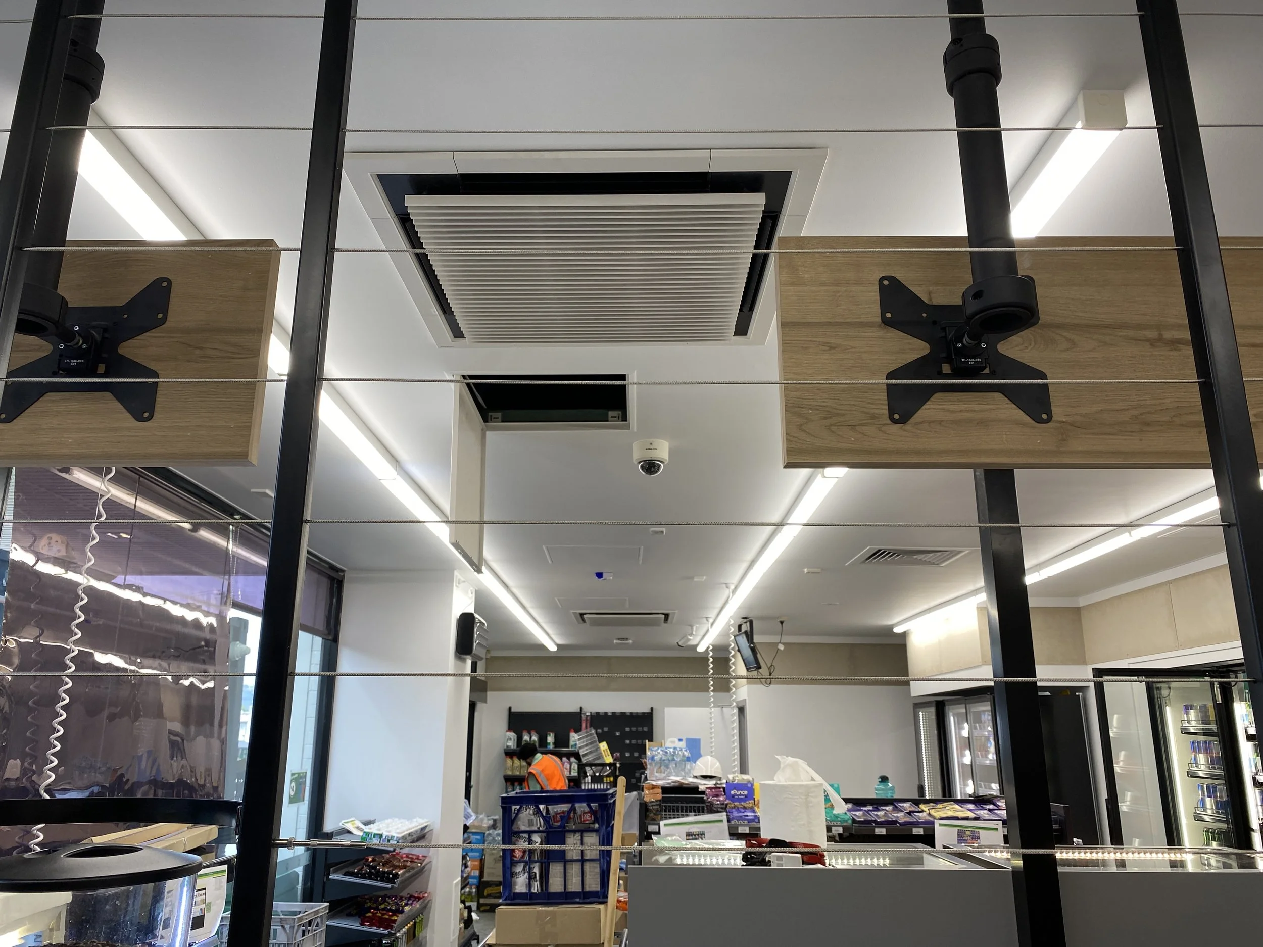 Interior of a convenience store or grocery store with checkout counters, shelves stocked with products, and a worker in an orange vest.