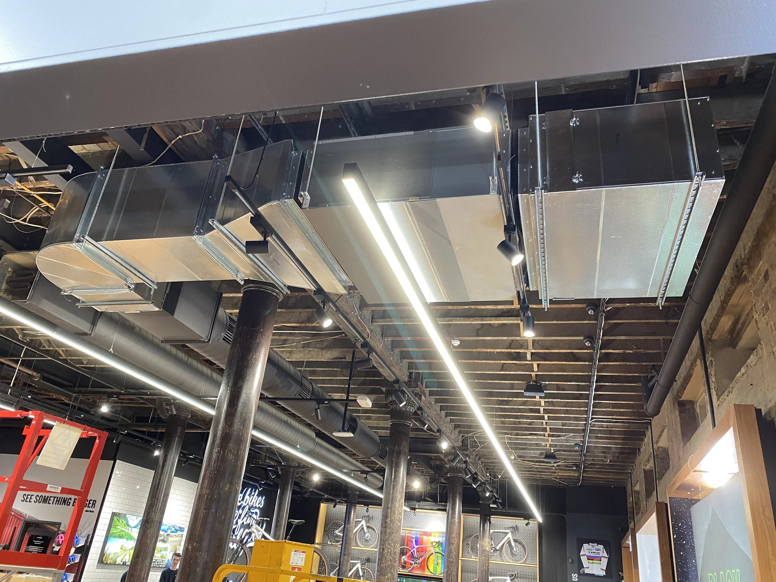 Interior of a retail store or showroom with exposed ceiling and industrial ductwork, featuring metallic architectural elements suspended from the ceiling.