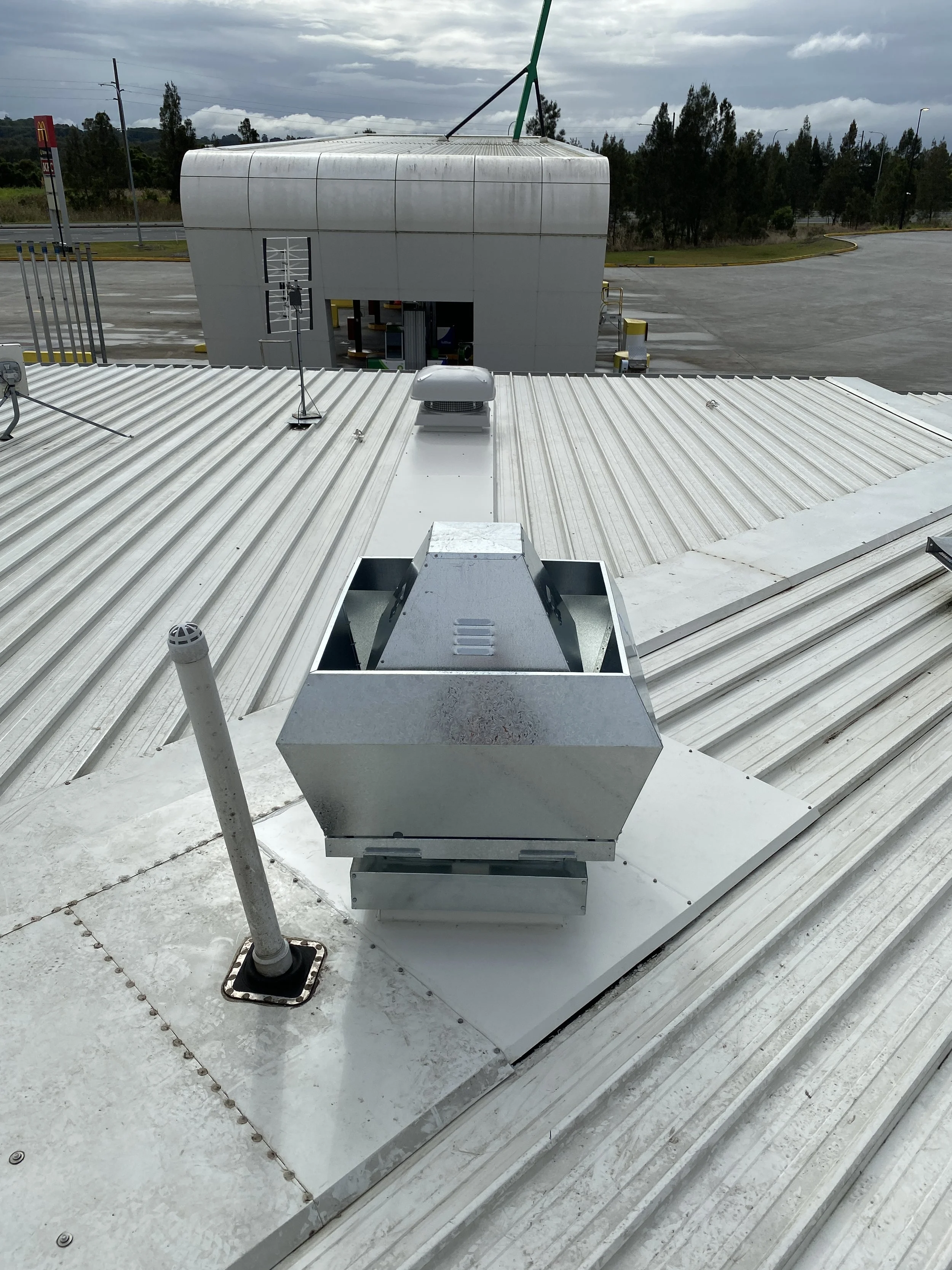 View of rooftop with HVAC unit and antennas, McDonald's sign in the background, parking lot, and cloudy sky.