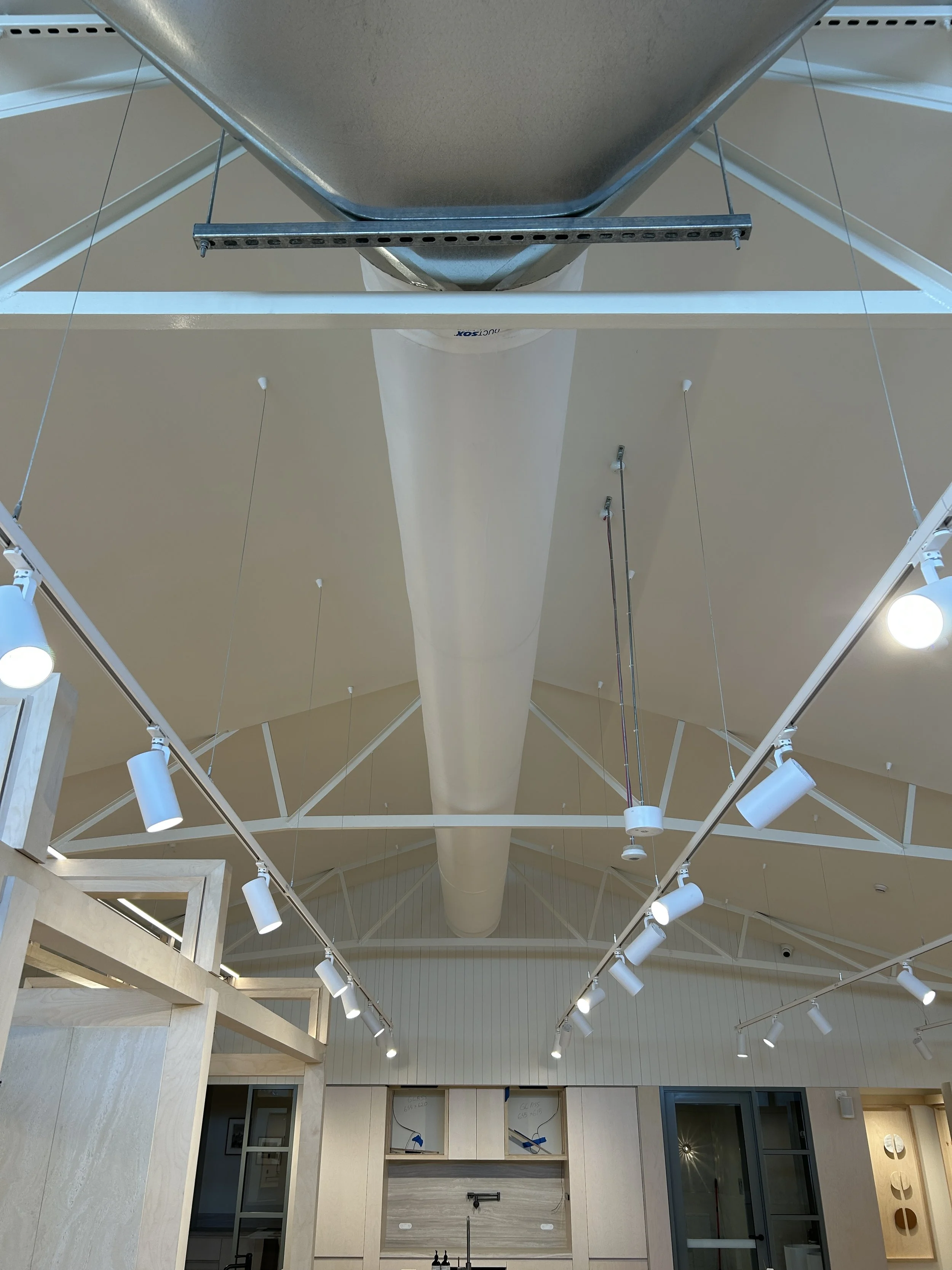 Ceiling view of an interior with a large central duct, track lighting, and exposed structural elements in a modern building.