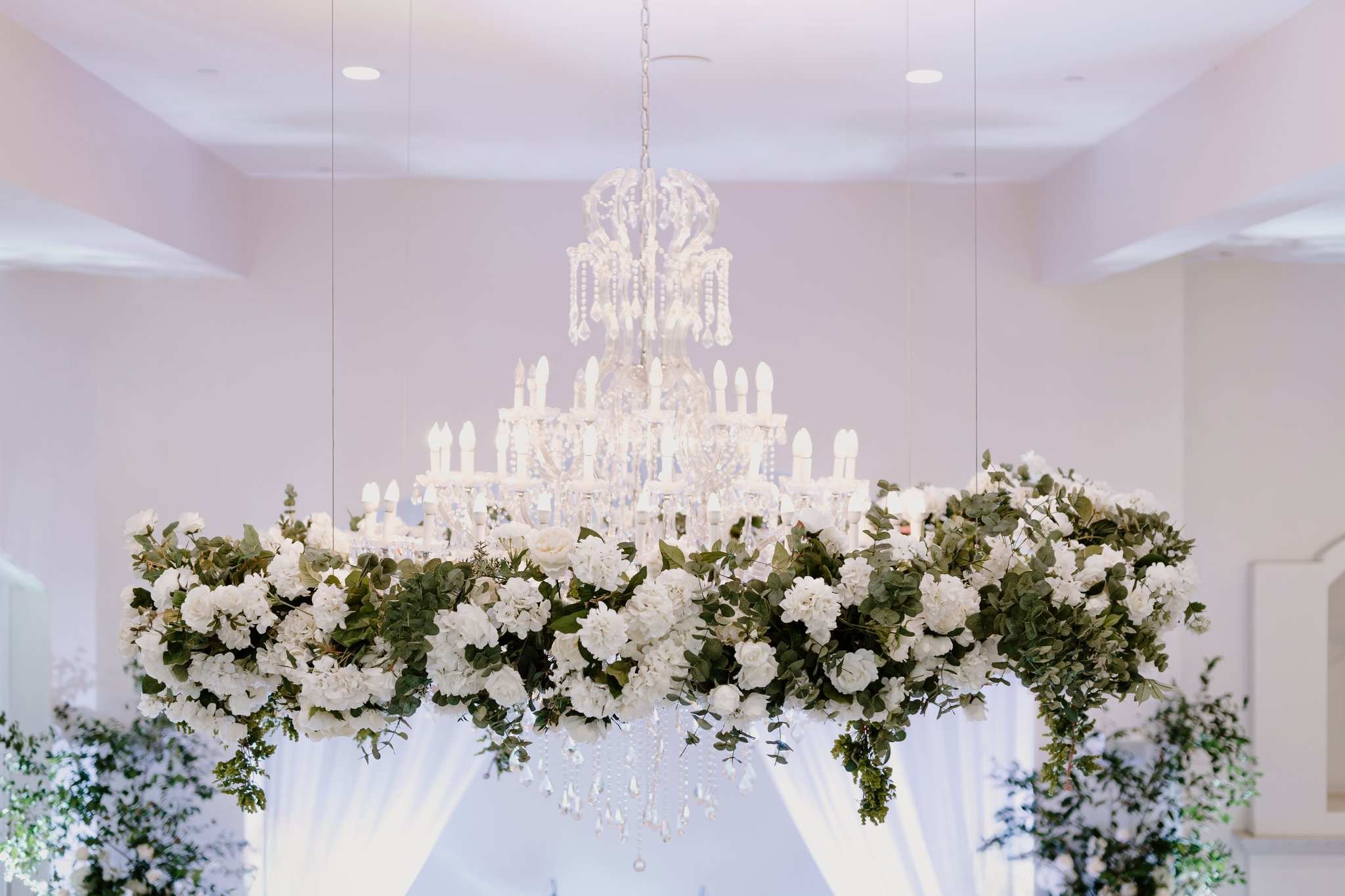 A large crystal chandelier hanging from the ceiling above a floral arrangement with white roses and greenery.