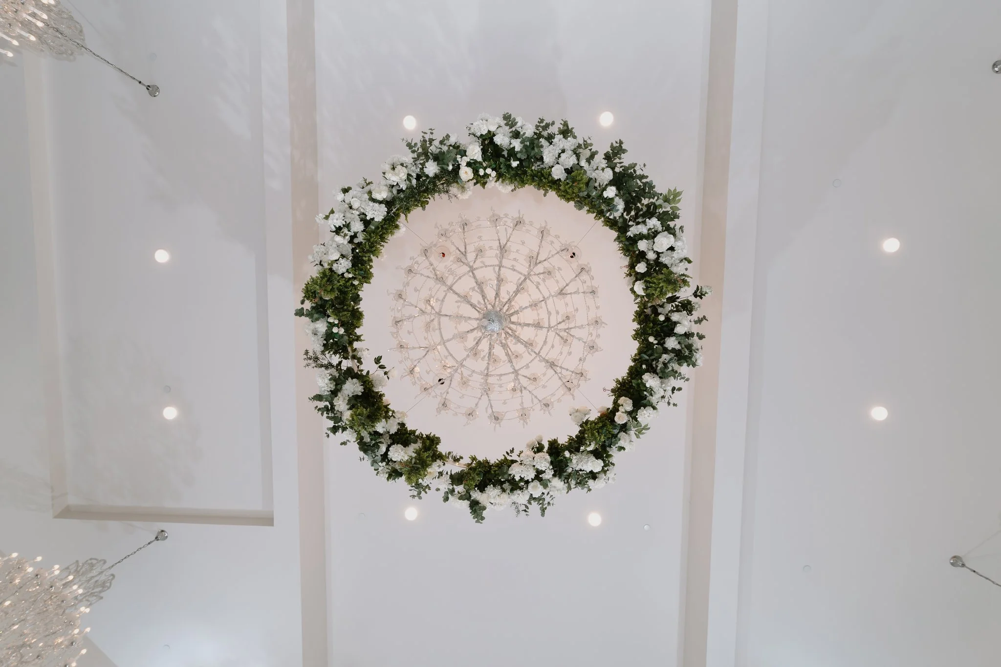 A ceiling decorated with a large circular floral arrangement and a chandelier, with small lights around.