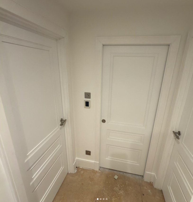 Three white doors and two wall switches in a corner, with a beige floor and white walls.