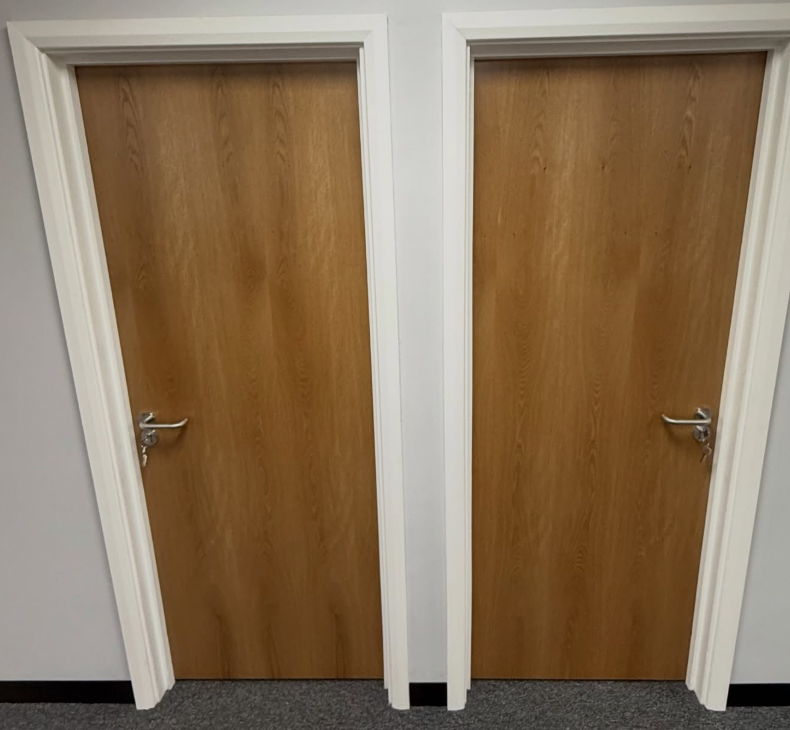 Two closed wooden doors in a hallway, one with a silver handle on the left, and the other with a silver handle on the right, separated by a white wall.