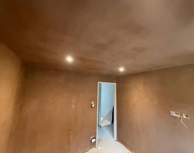 Empty room with brown walls and ceiling, two recessed lights, doorway to hall with staircase, and some electrical outlets and wires.