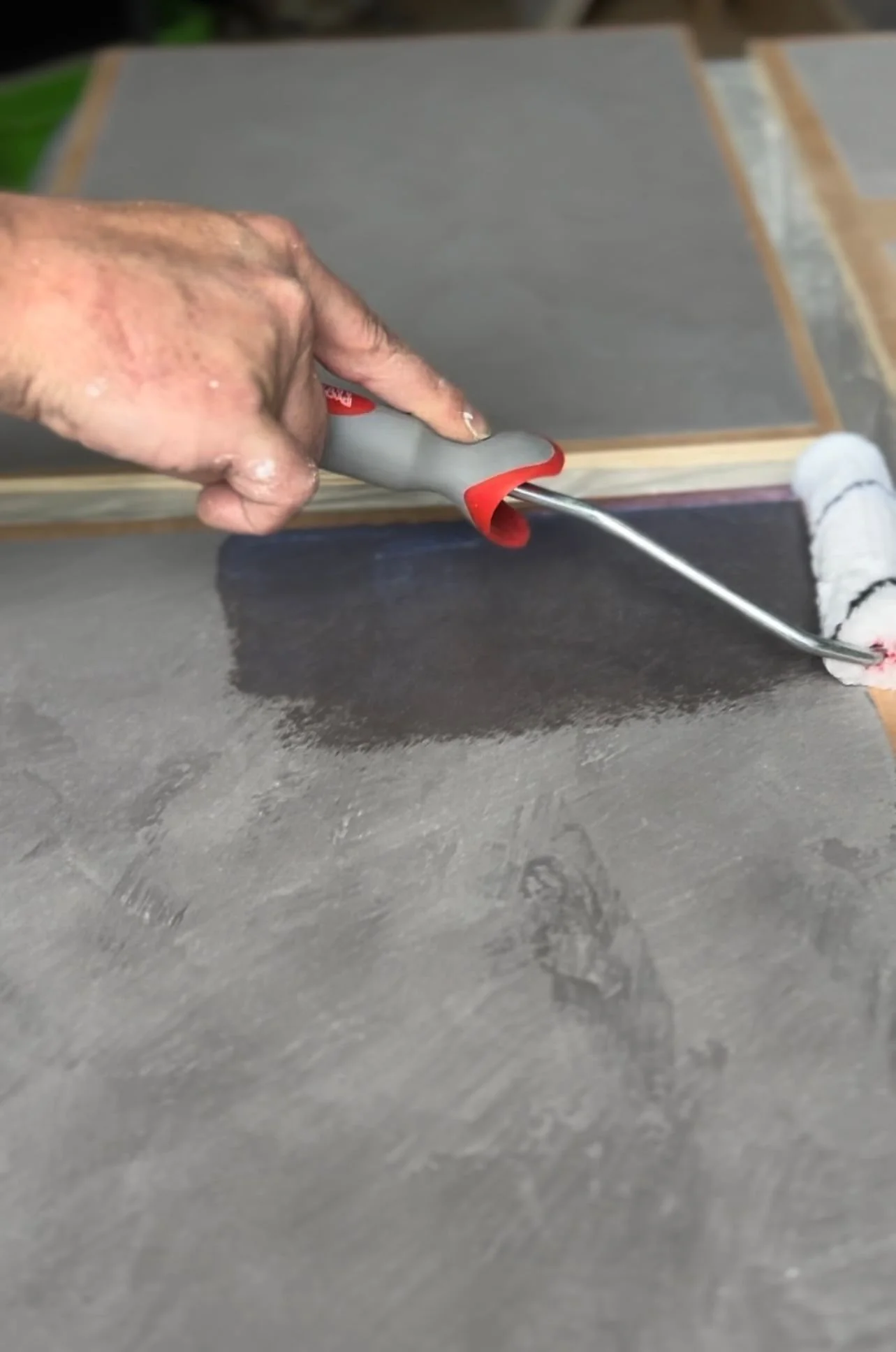 A person painting a surface with a roller brush, using a paint roller on a black painted area.