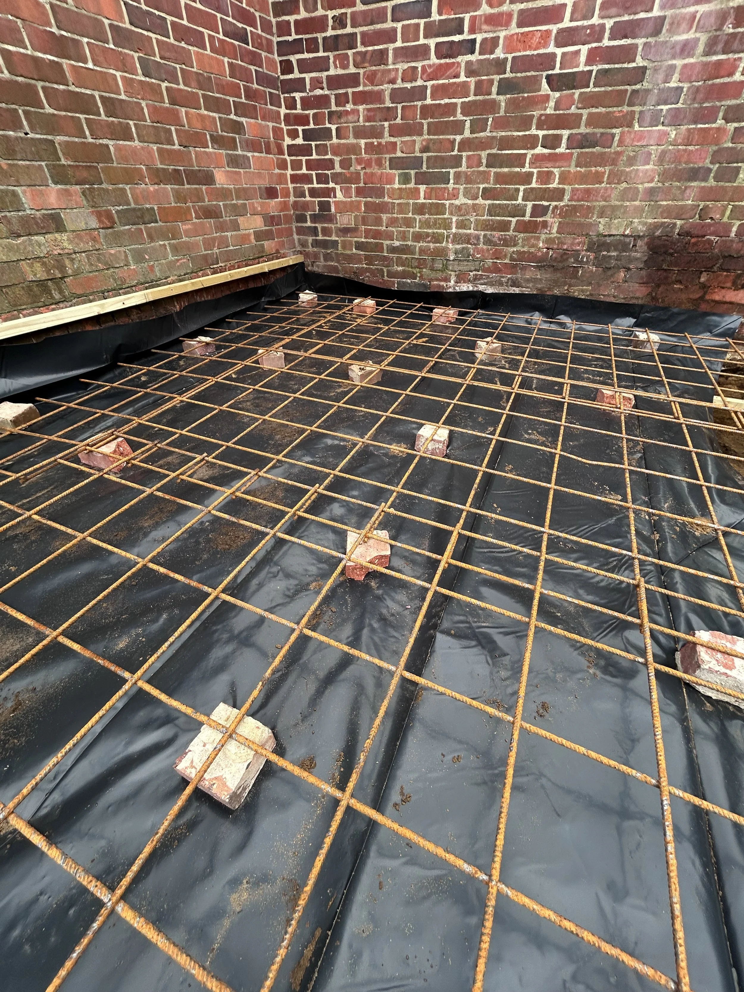 Resealed roof with exposed metal rebar grid, brick walls, and black waterproofing liner.