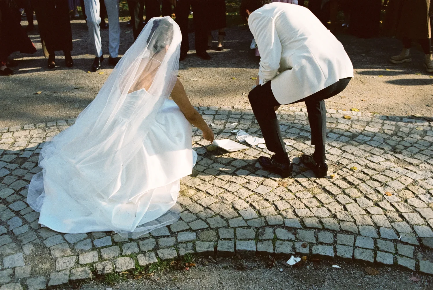 Close-up of bride and groom interacting on the ground, focus on 35mm film grain and dress texture.