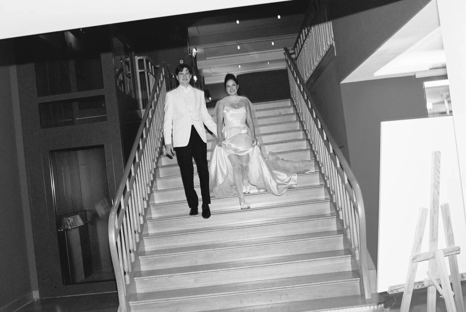A grainy B&W shot of Munira and Felix descending a grand staircase, a documentary-style wedding entrance.