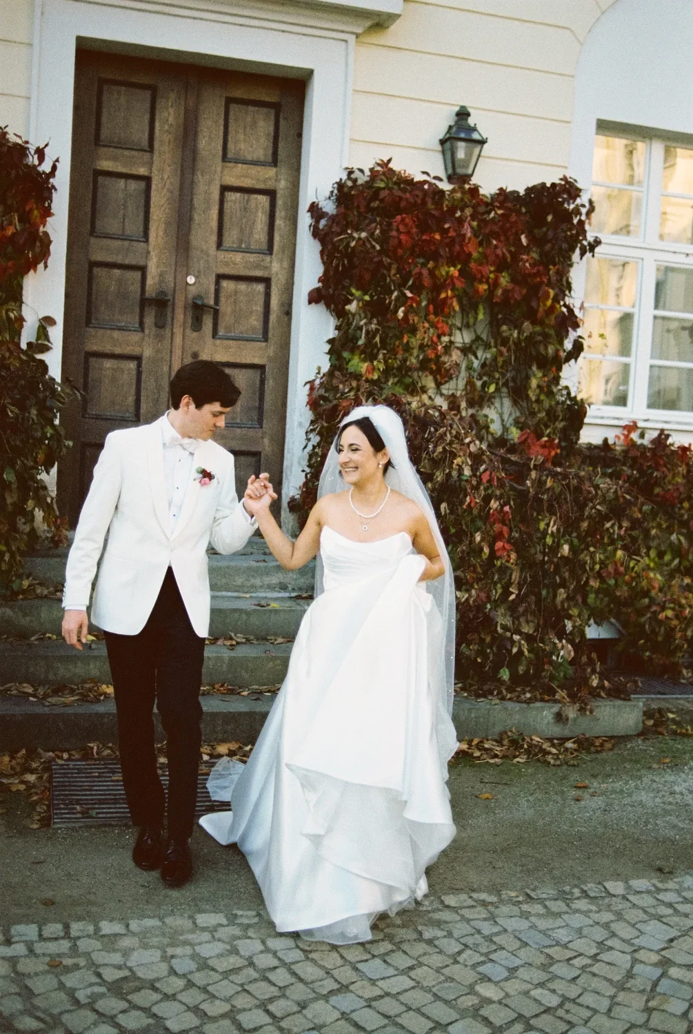 Documentary black and white 35mm portrait of a couple on old stairs surrounded by grapevines next to a wooden door at Schloss Lübbenau.