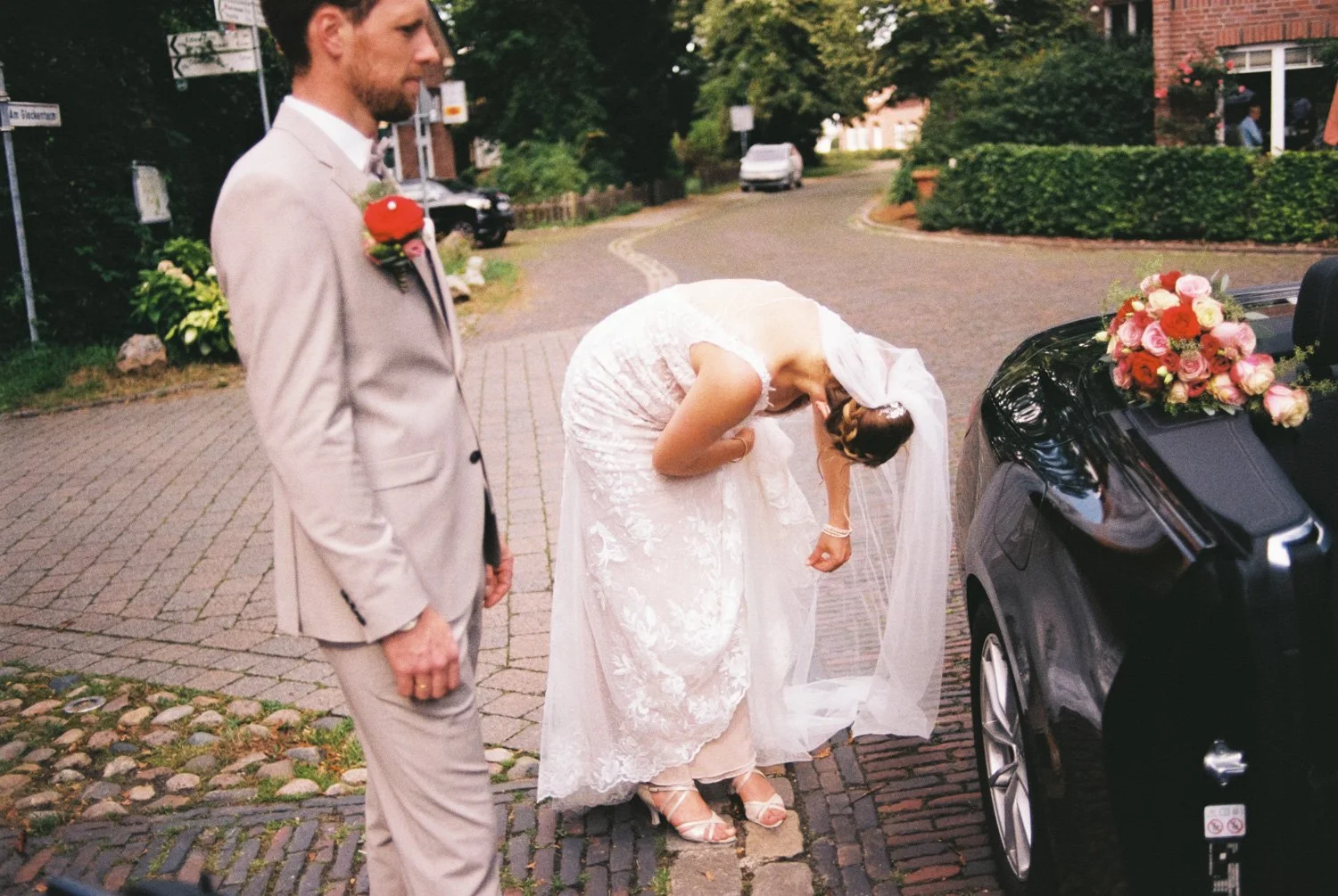 Bride in vintage lace dress adjusts shoe, groom nearby, captured with analog wedding photography charm