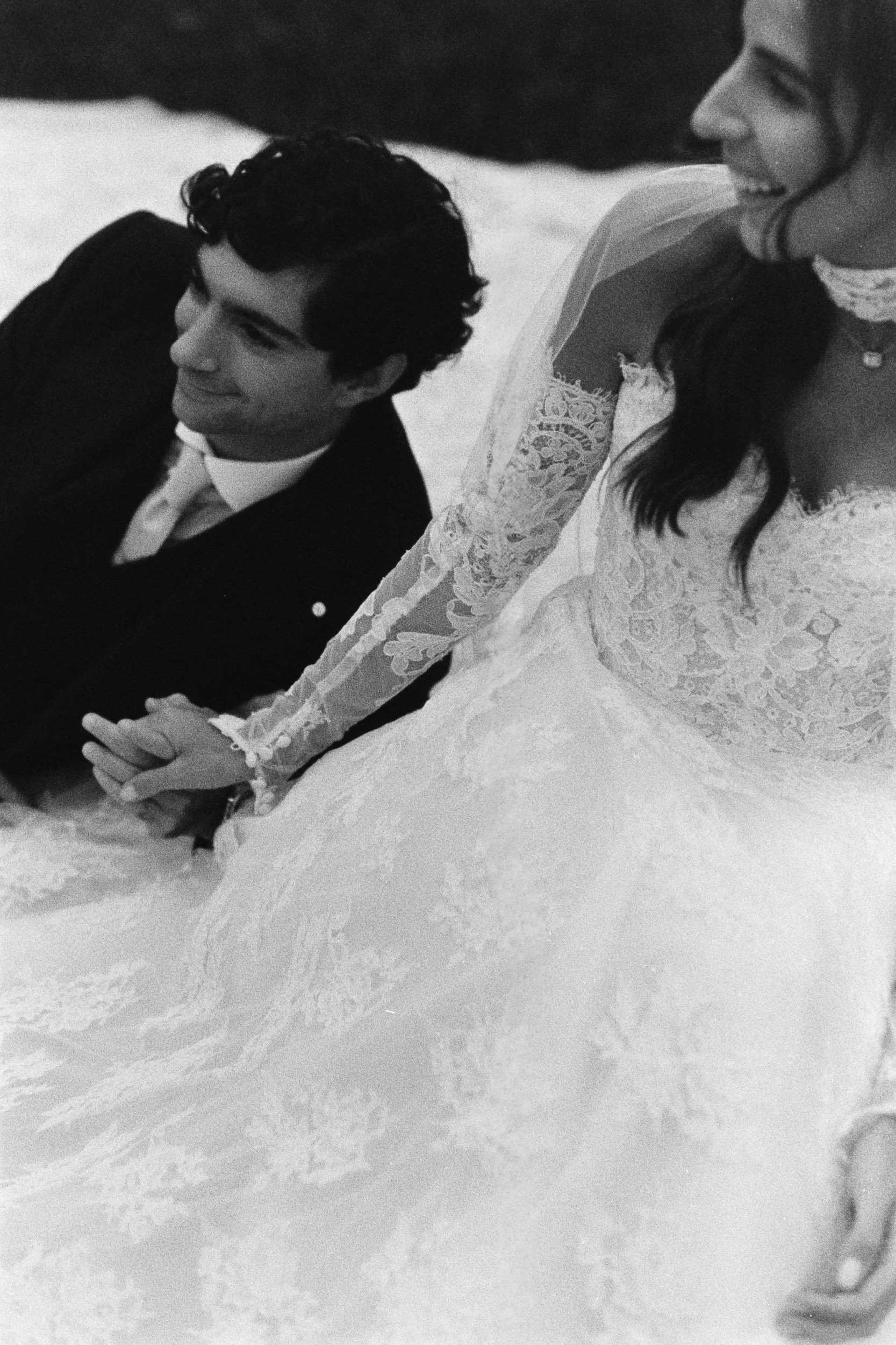 High-grain black and white close-up of a bride and groom holding hands and laughing on the ground.