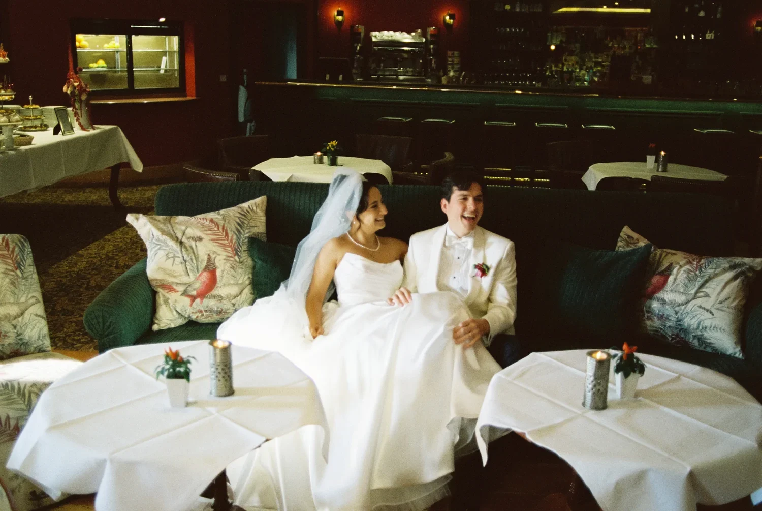 Bride and groom laughing together on a green velvet sofa in the red salon, authentic unposed wedding photography.