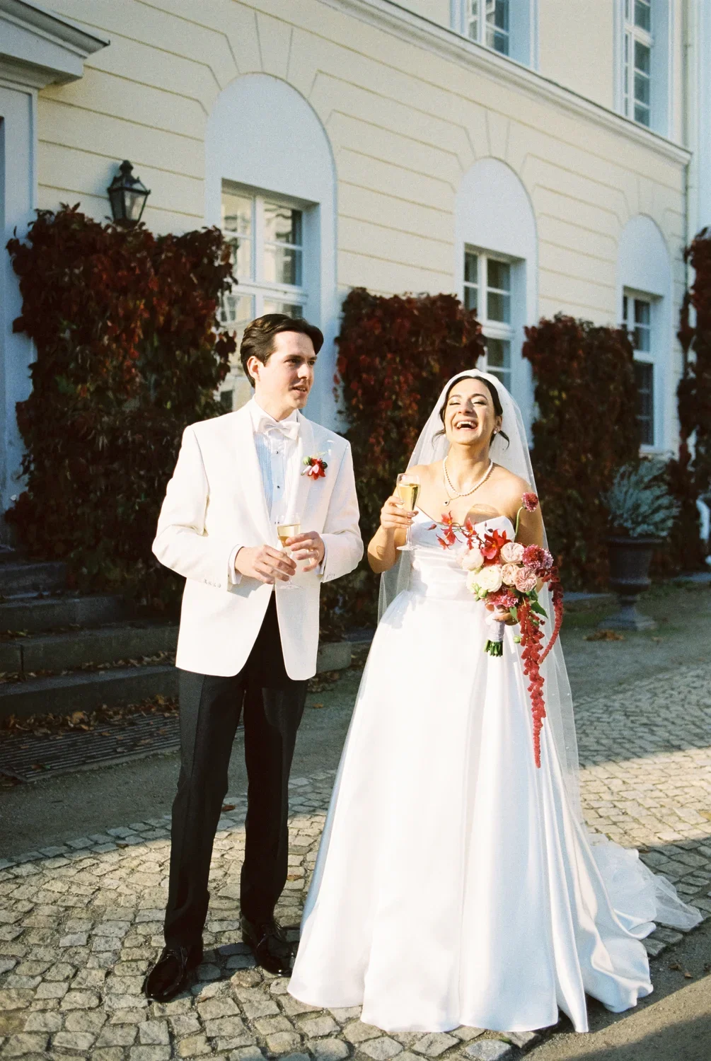 Candid shot of bride and groom laughing with champagne glasses in front of Schloss Lübbenau, 35mm film.