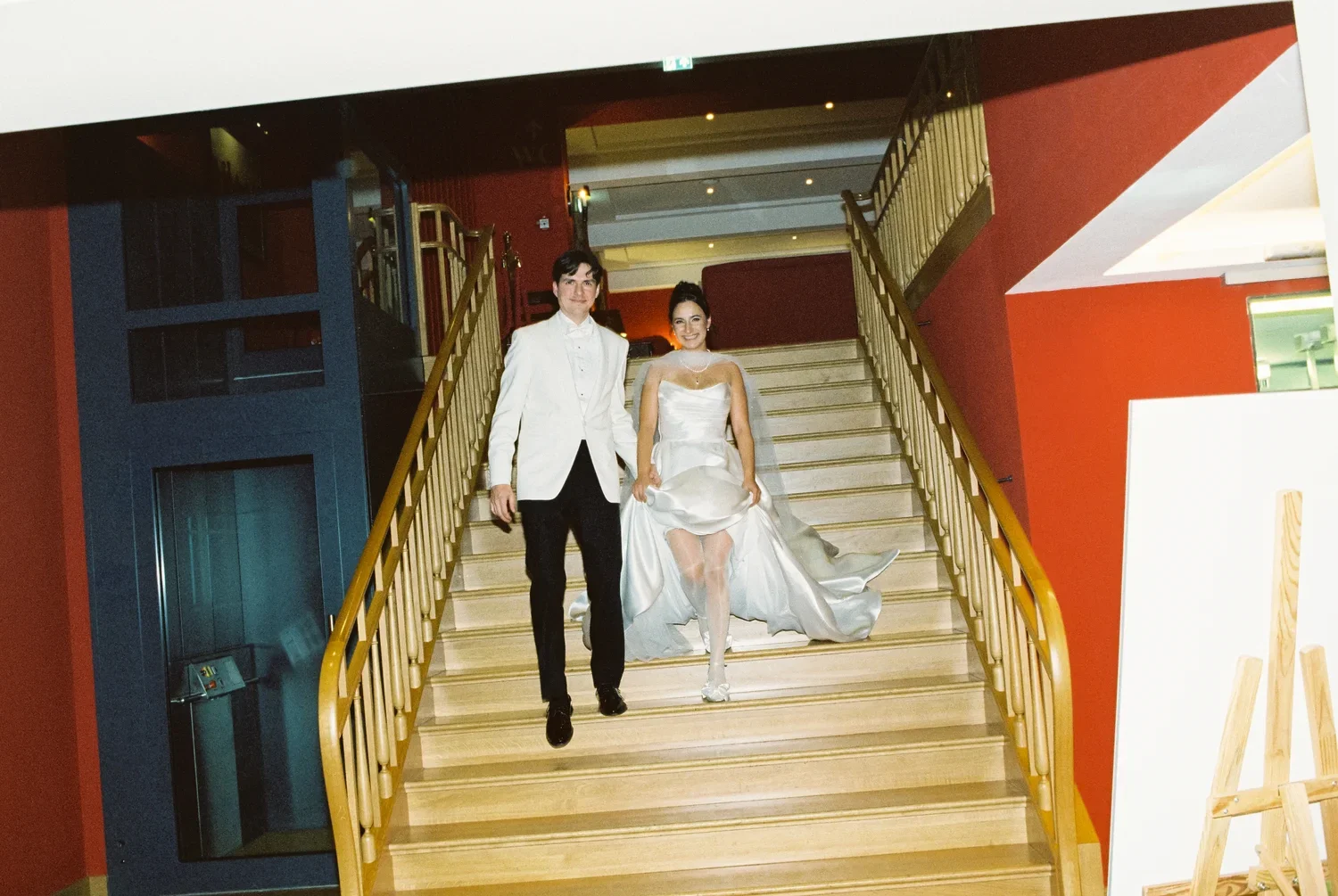 Color film shot of a couple entering a historic ballroom with red walls, highlighting the raw flash aesthetic.