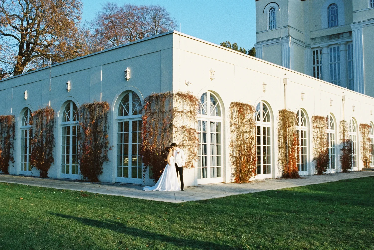 Wide-angle shot of a couple kissing in front of the long white facade with arched windows at Schloss Lübbenau.