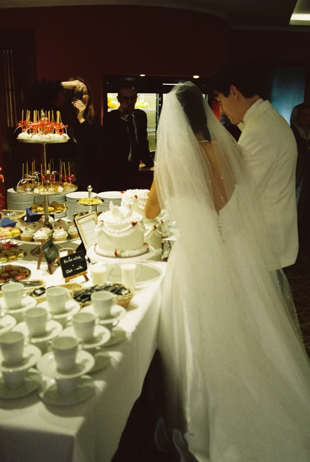The couple standing at the cake buffet with coffee cups in the foreground, capturing the afternoon's social energy.