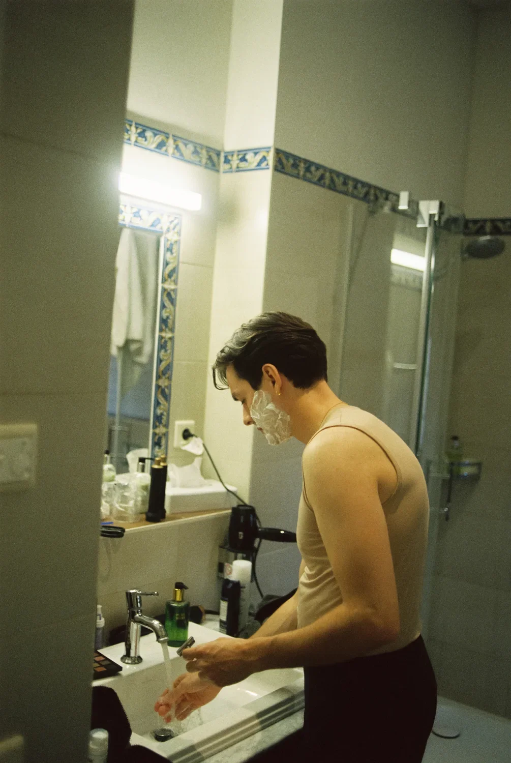 Raw documentary shot of a groom shaving in a bathroom mirror, authentic 35mm film grain.