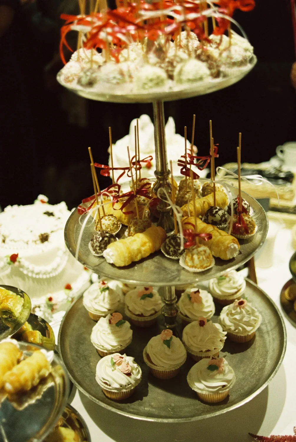 Close-up of a silver tiered stand filled with cupcakes and cream horns, rustic wedding dessert documentary.